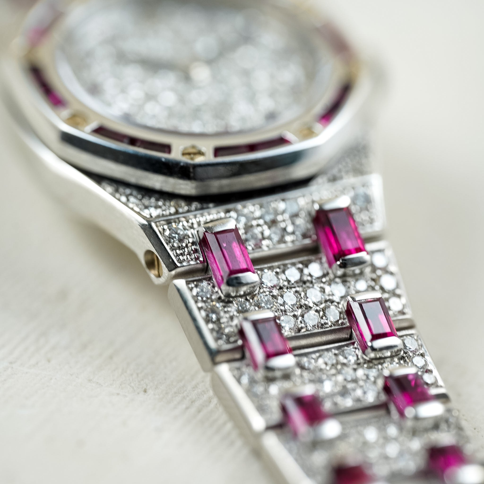 Close-up of a watch with pink gemstones and diamond-studded band on a light background