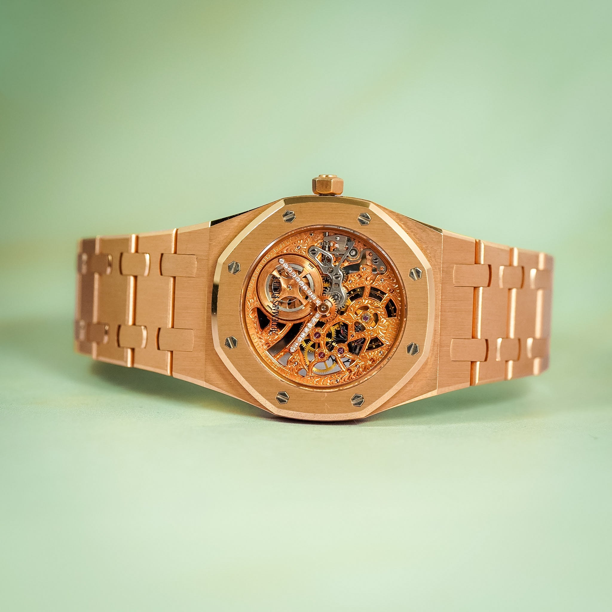 A rose gold automatic watch with a skeleton dial, featuring visible internal gears and a matching rose gold link bracelet, set against a soft mint green background.