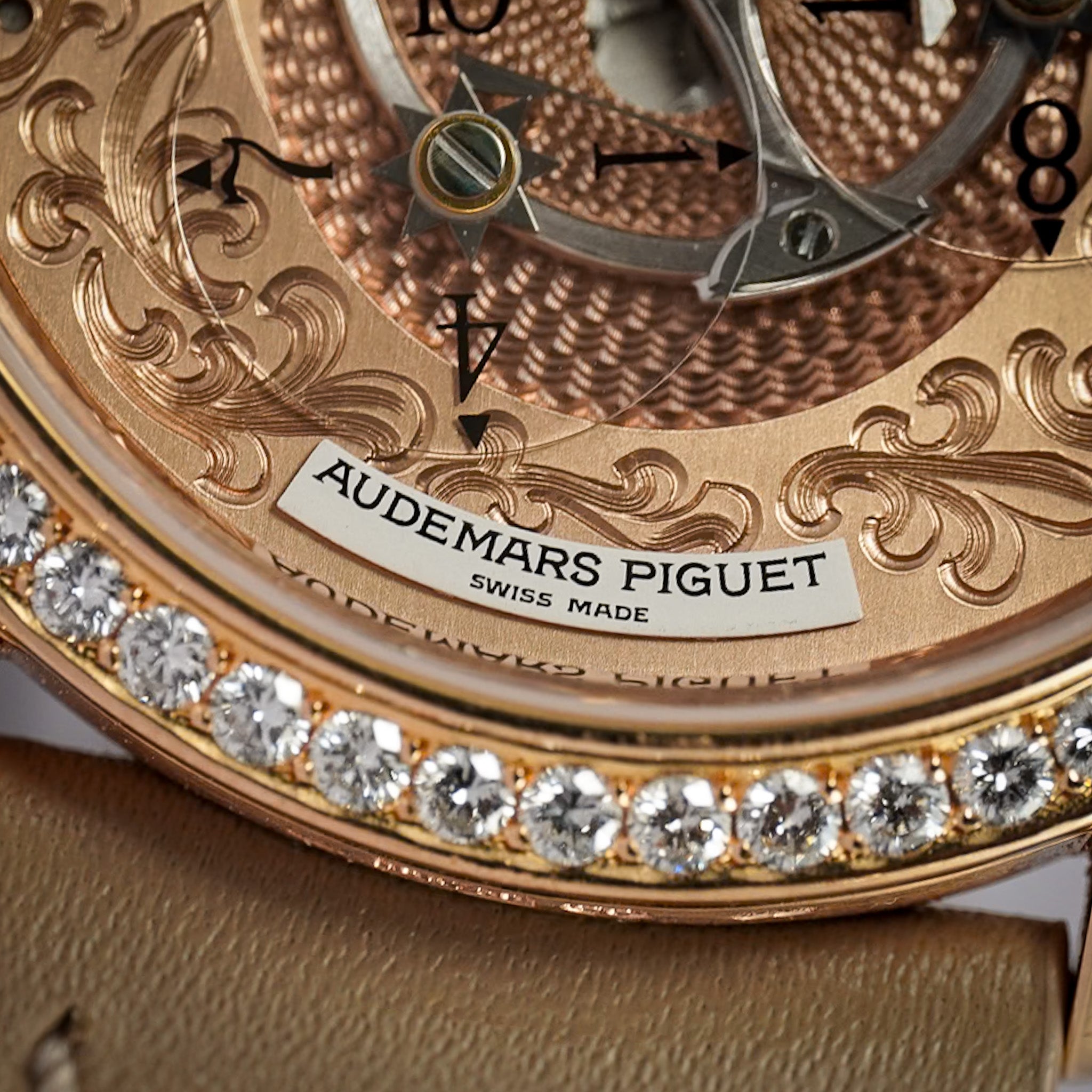 Close-up of an Audemars Piguet watch featuring an ornate rose gold skeleton dial, a bezel set with clear crystals, and a textured gold-toned strap.