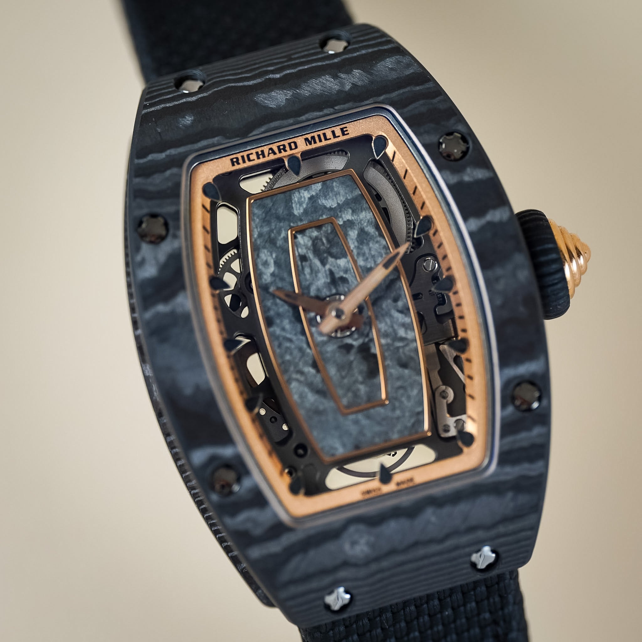 Richard Mille wristwatch with a dark gray marbled ceramic case, a skeleton dial showing the inner movement, rose gold-toned hands and case accents, and a black fabric strap on a beige background.