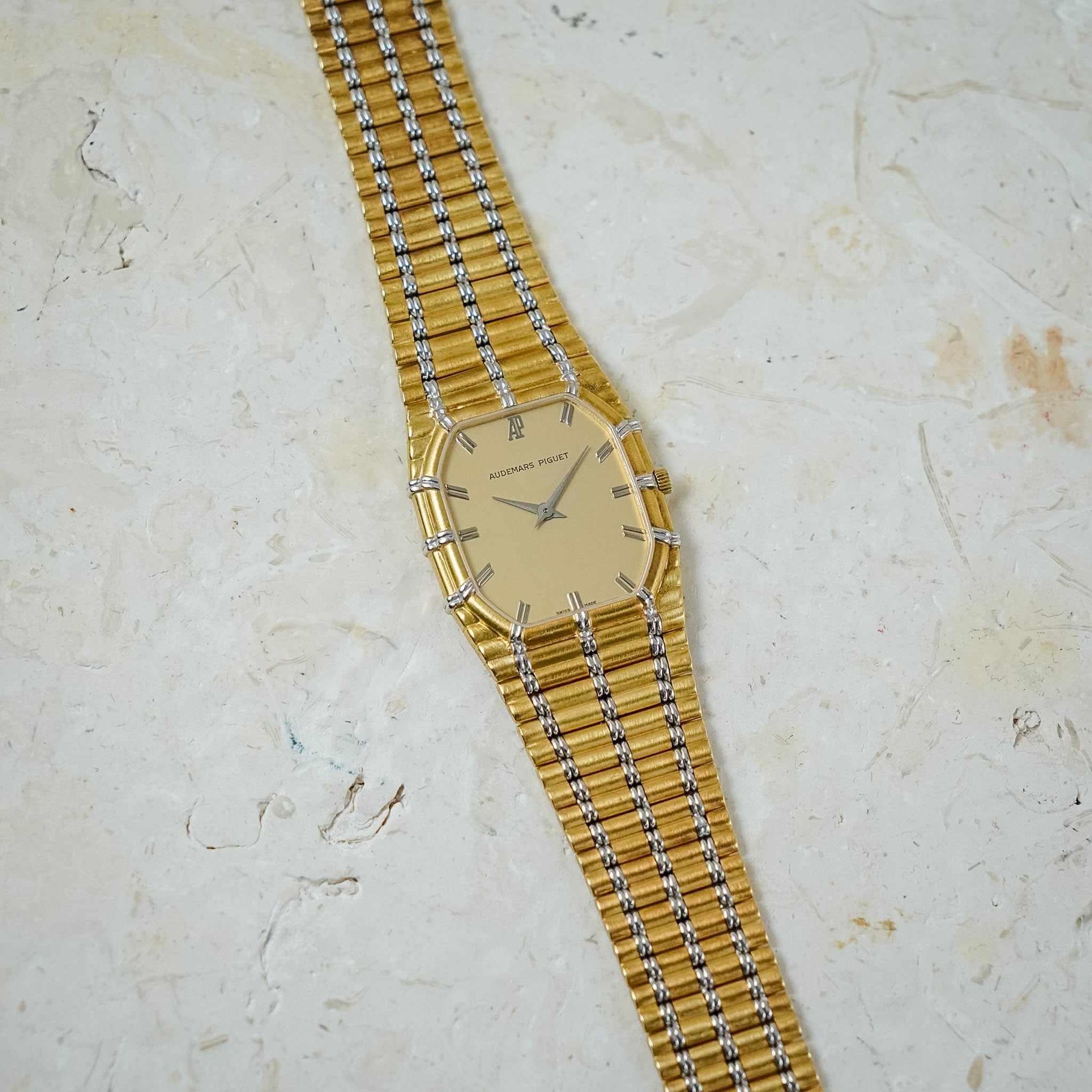 An Audemars Piguet Bamboo in yellow gold and white gold with a gold dial, shot laying flat on a light stone table