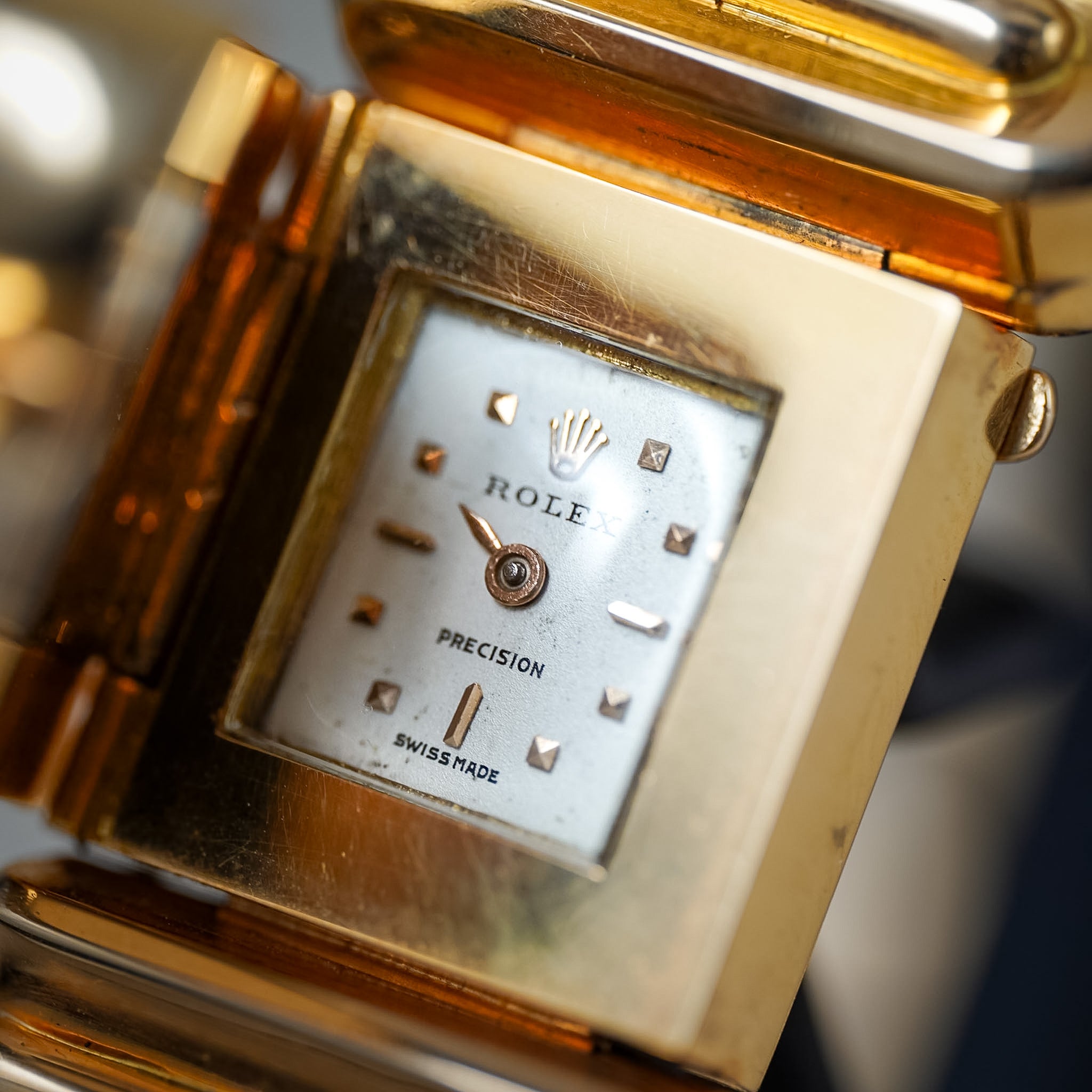 Close-up of a gold-tone Rolex wristwatch with a silver dial and visible Rolex crown logo, showing the brand name 'Rolex' and 'Precision Swissmade'.