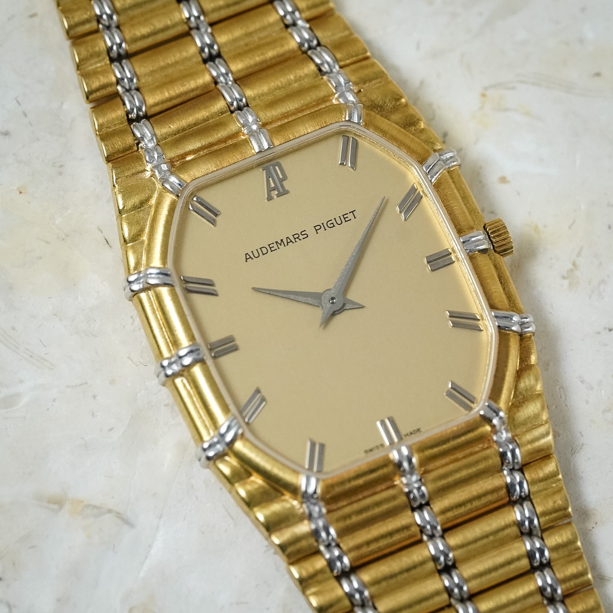 Close-up of an Audemars Piguet Bamboo in yellow gold and white gold with a gold dial, shot on a light stone table