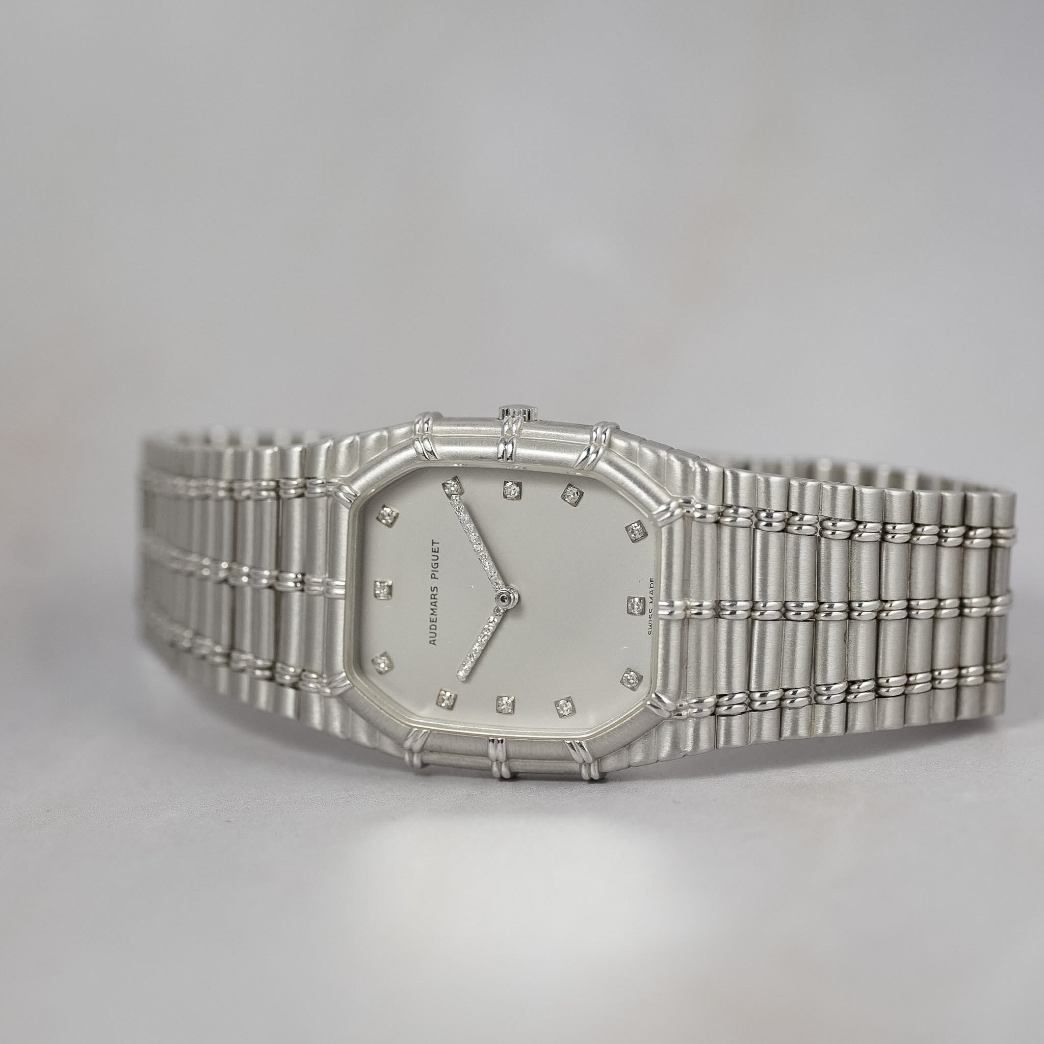 A silver-toned Cartier Santos watch with a diamond-dusted bezel, white dial, and matching stainless steel link bracelet, photographed on a light gray background.