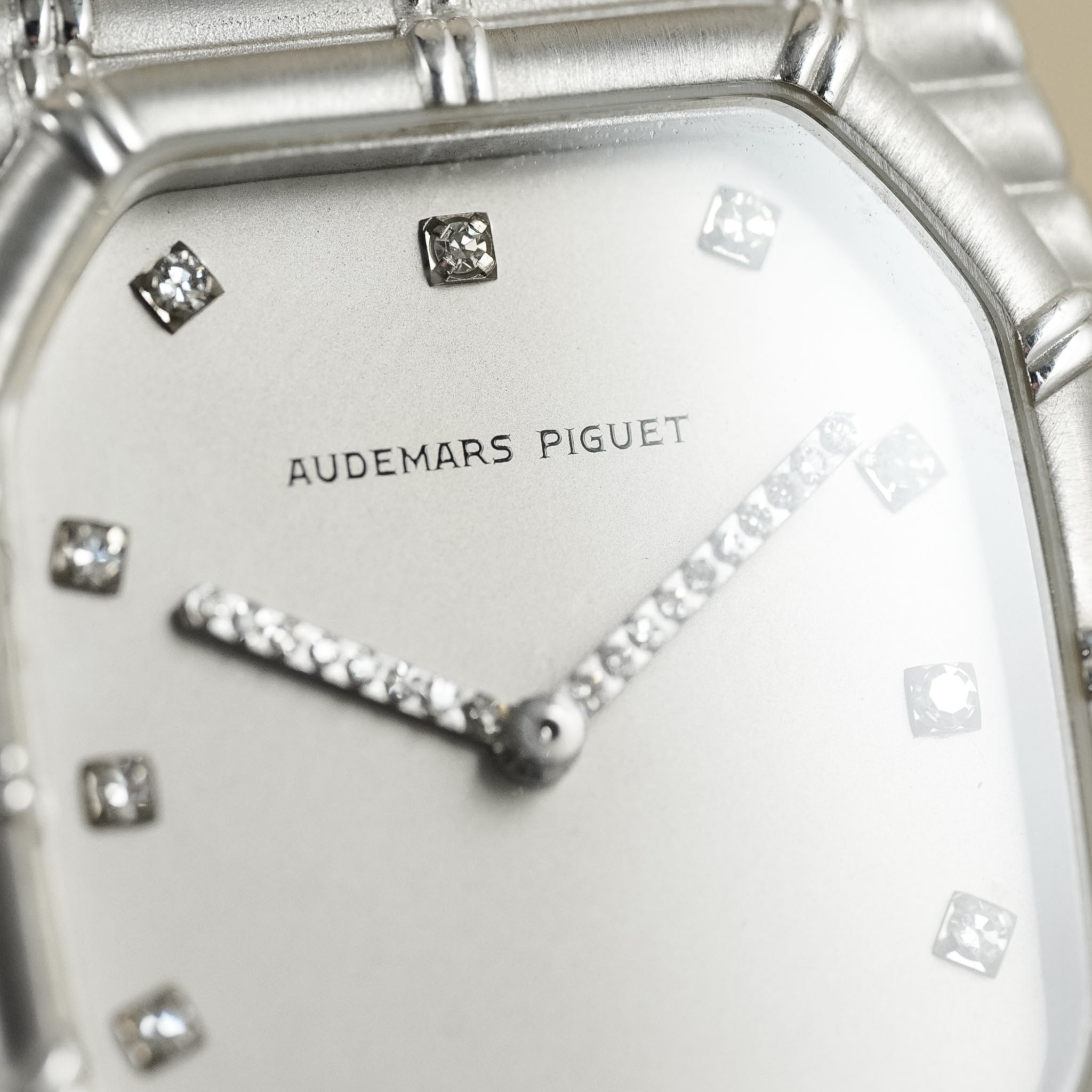 Close-up of an Audemars Piguet watch dial and bracelet, showing a silver-toned case, white dial, diamond hour markers, and diamond hands.