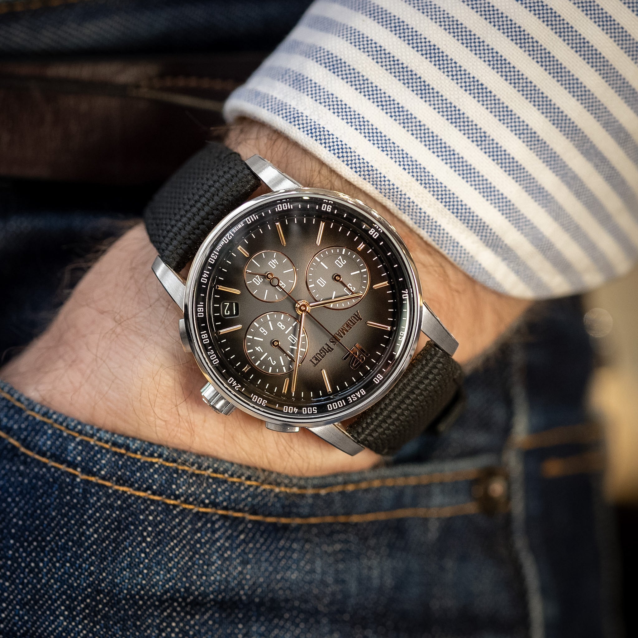 Close-up of a wrist wearing a stylish watch with a detailed face, set against a denim background.