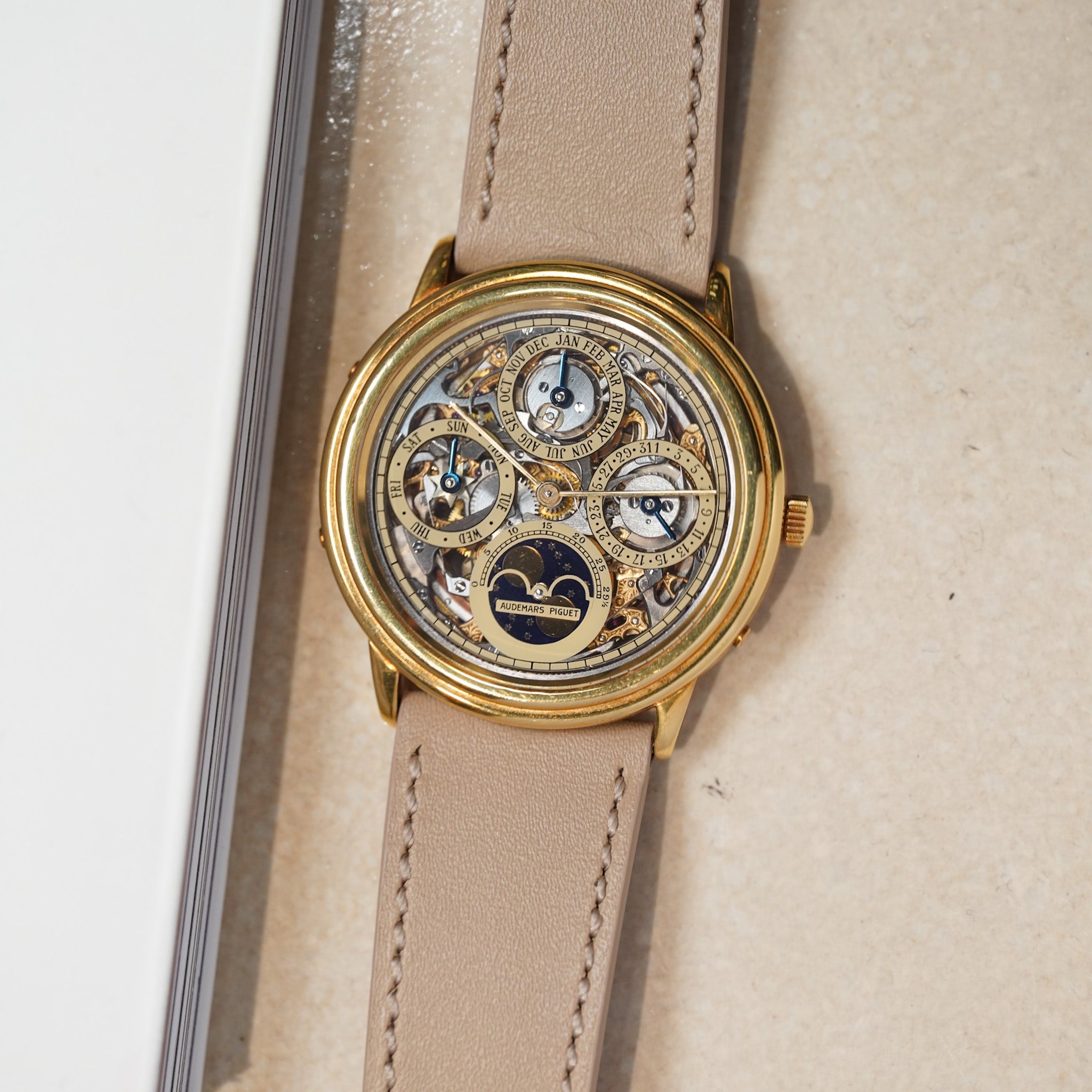 Gold wristwatch with a beige leather strap on a light background