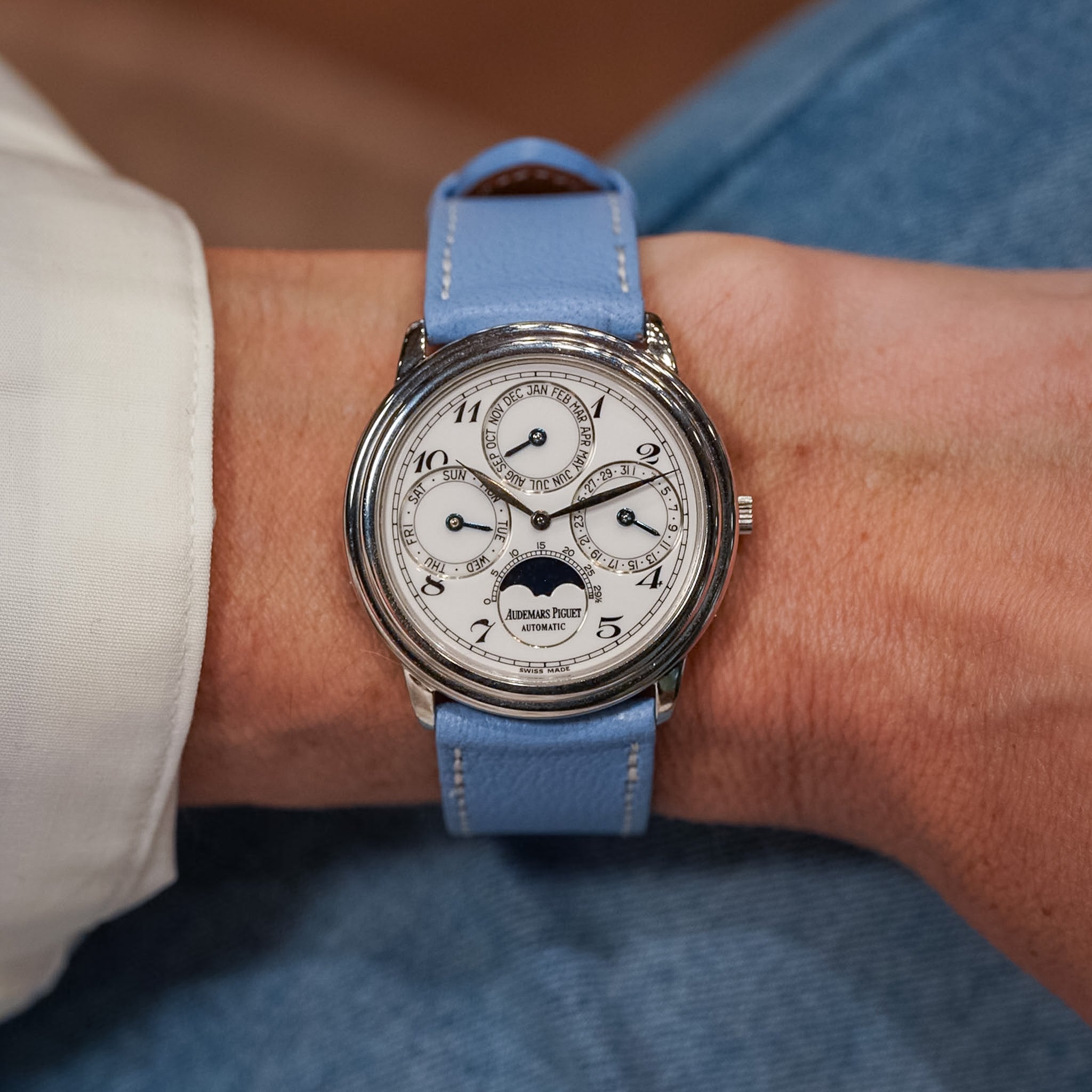 Vintage wristwatch with a blue strap on a person's wrist, wearing a light-colored shirt and blue jeans.