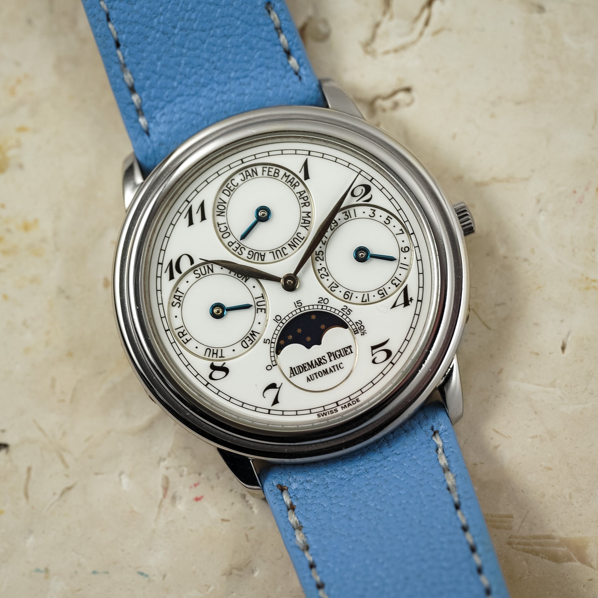 Watch with blue leather strap on a textured beige background