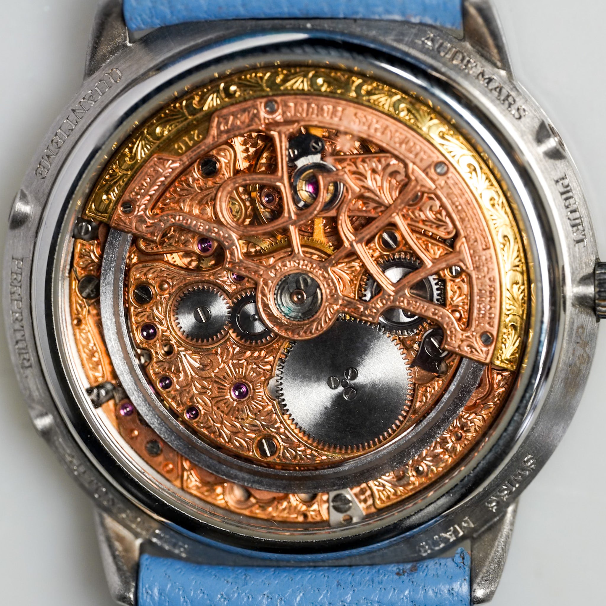 Close-up of a mechanical watch with intricate gears and blue strap on a light gray background