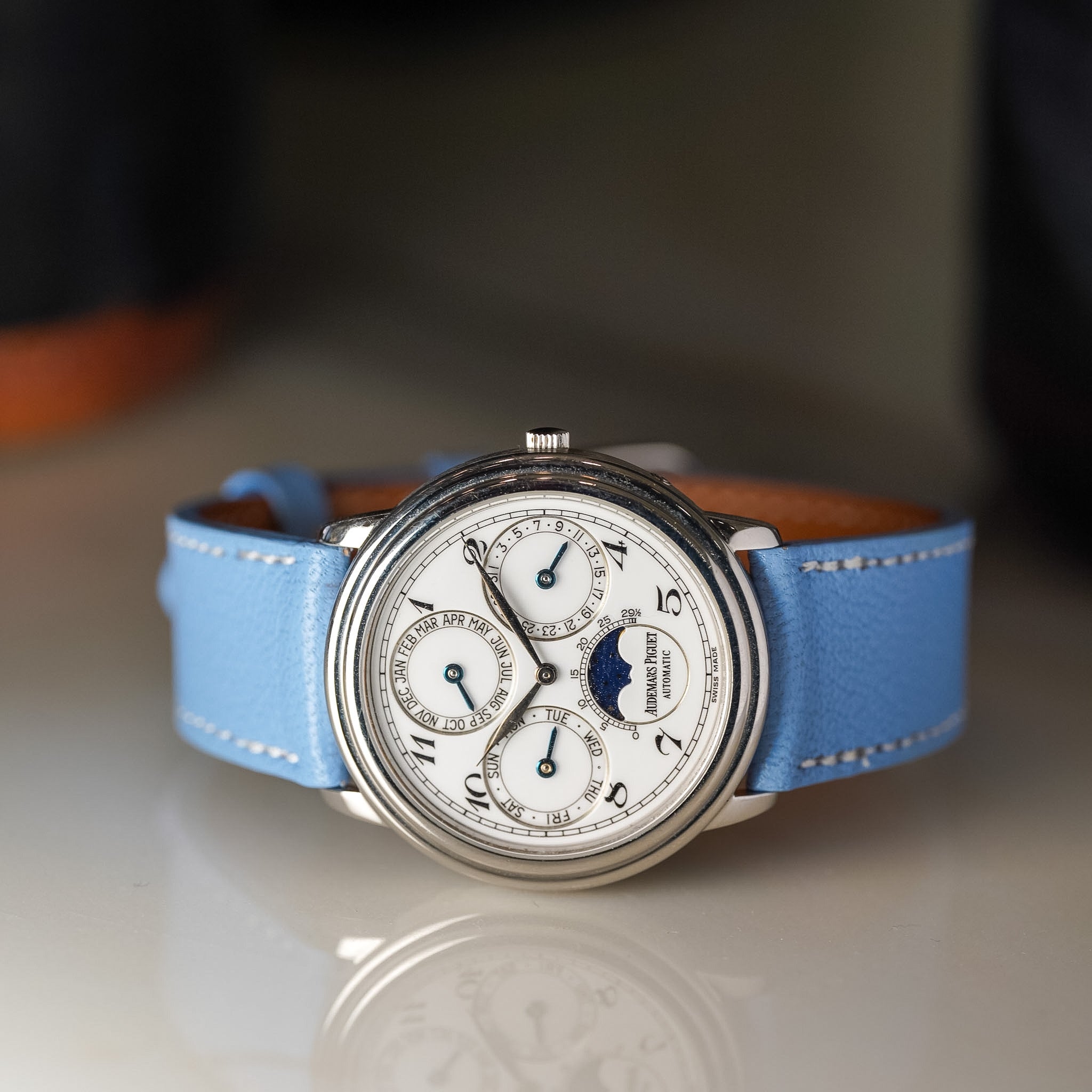 Wristwatch with blue strap on a reflective surface