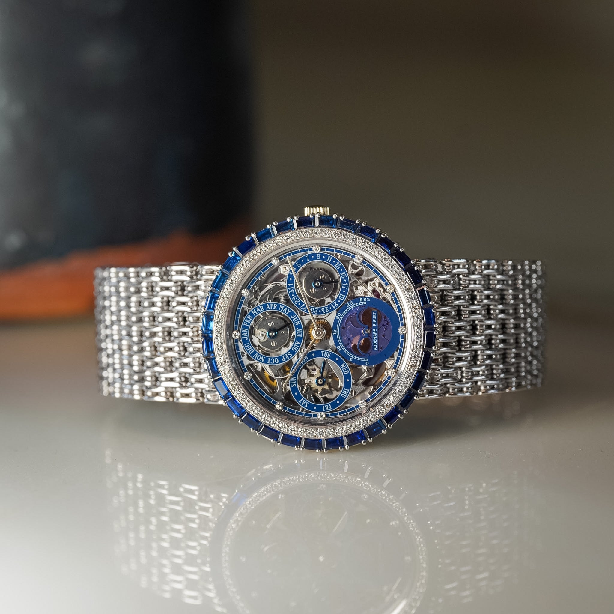Luxury watch with intricate design and blue accents on a reflective surface