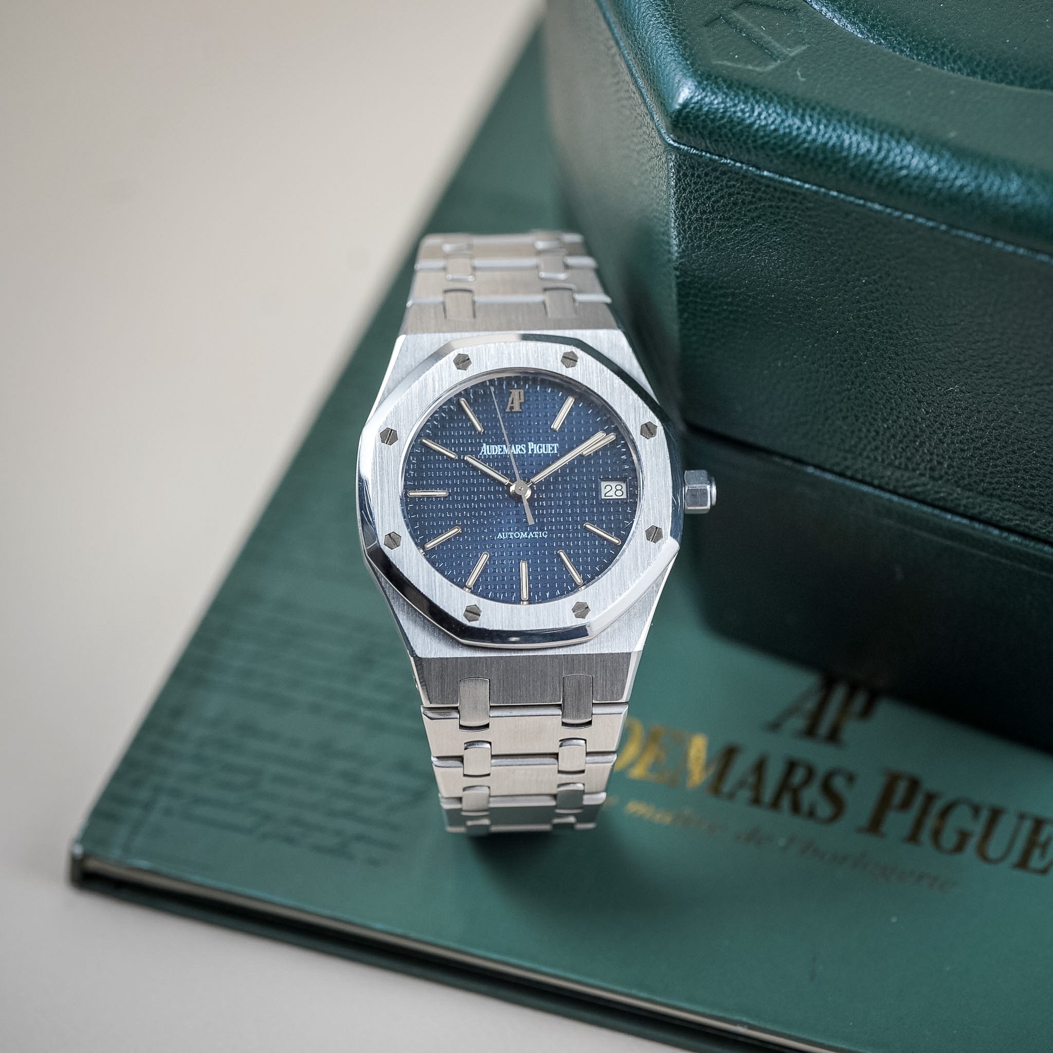 Luxury watch with blue face and silver metal strap on a green box with Audemars Piguet branding.