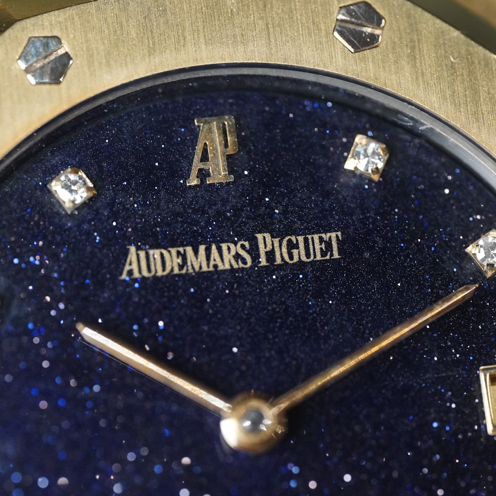 Close-up of a watch face with 'Audemars Piguet' branding on a blue glittery background.