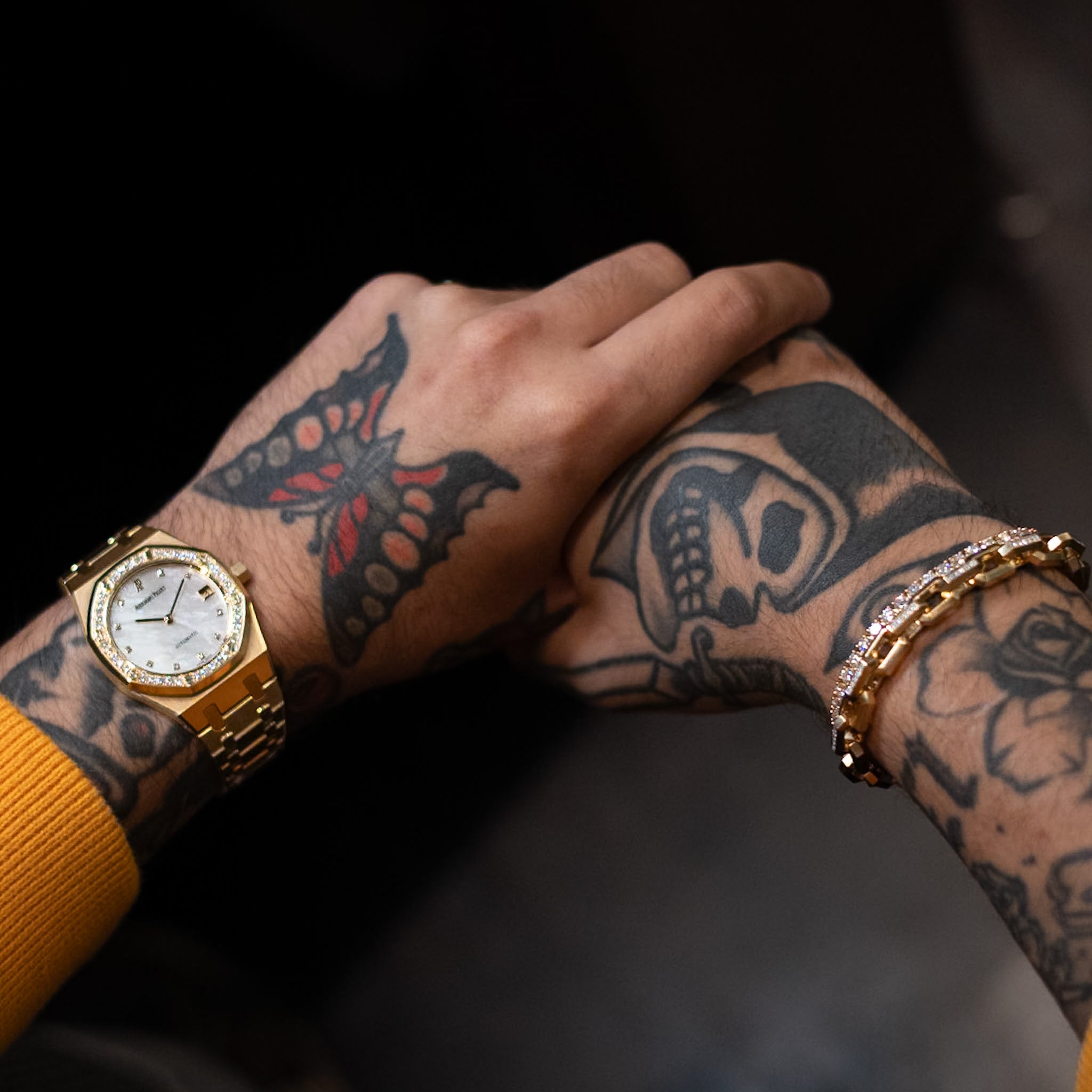 Gold watch on a wrist with tattoos against a dark background