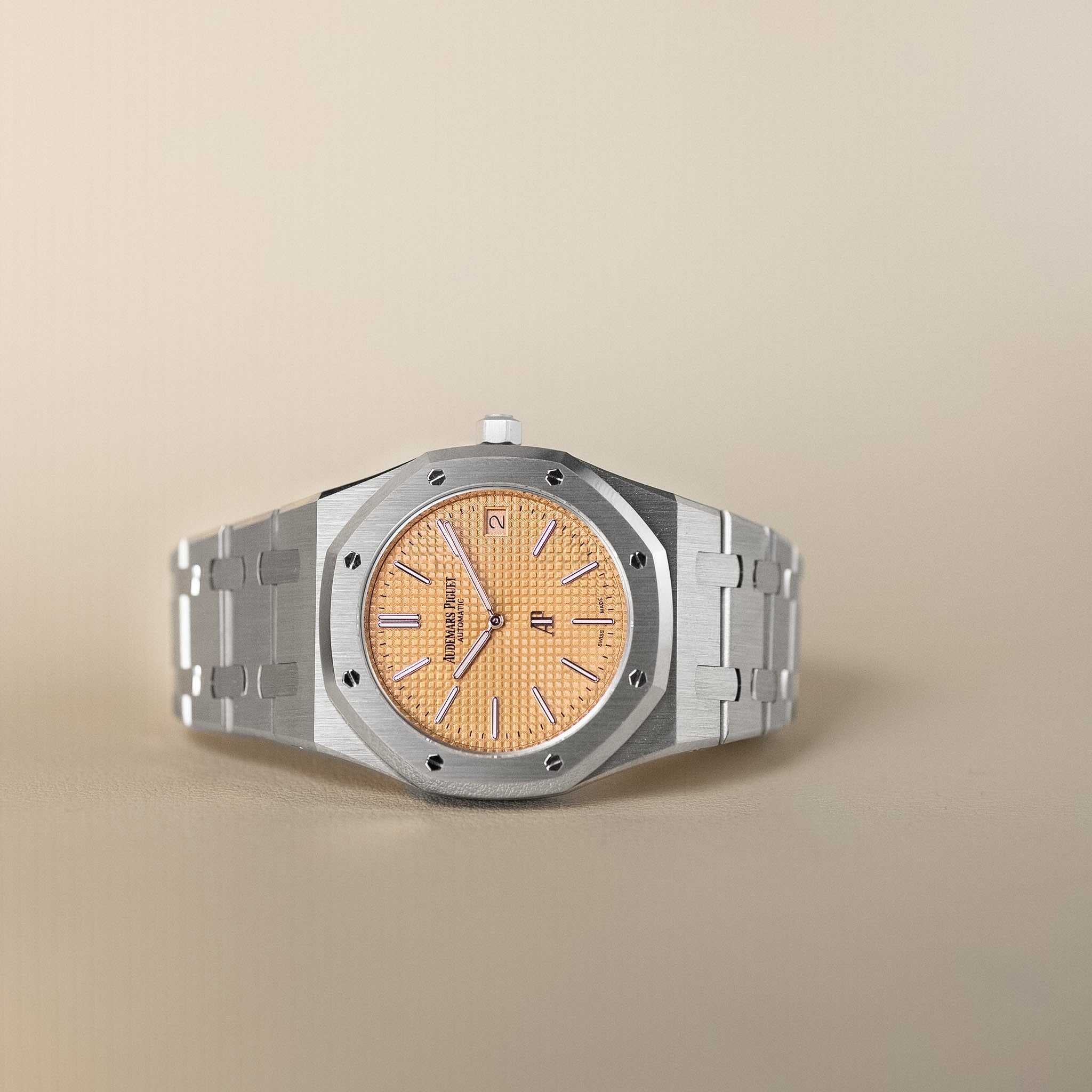 Luxury watch with a gold face and silver case on a beige background