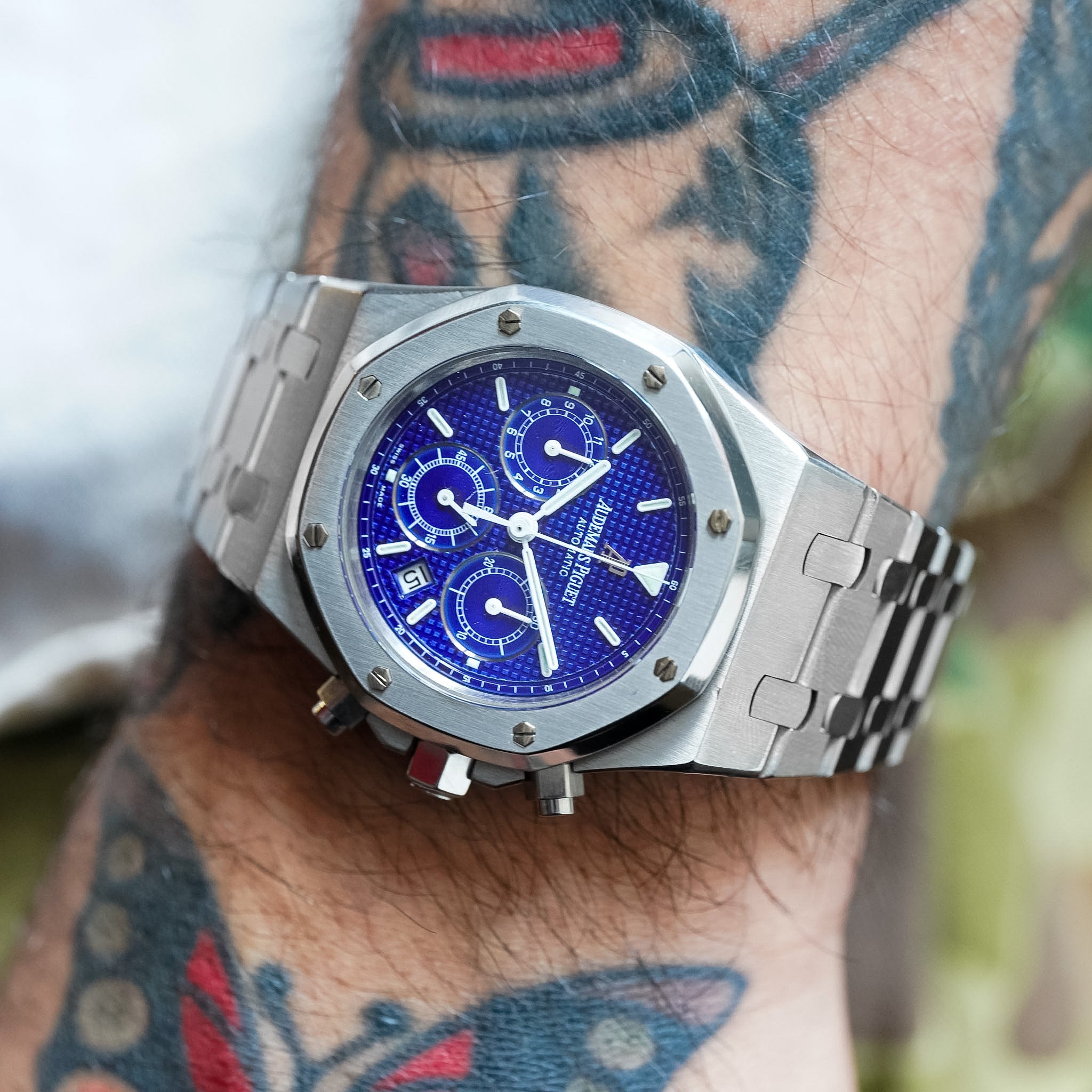 Silver watch with a blue face on a wrist with tattoos
