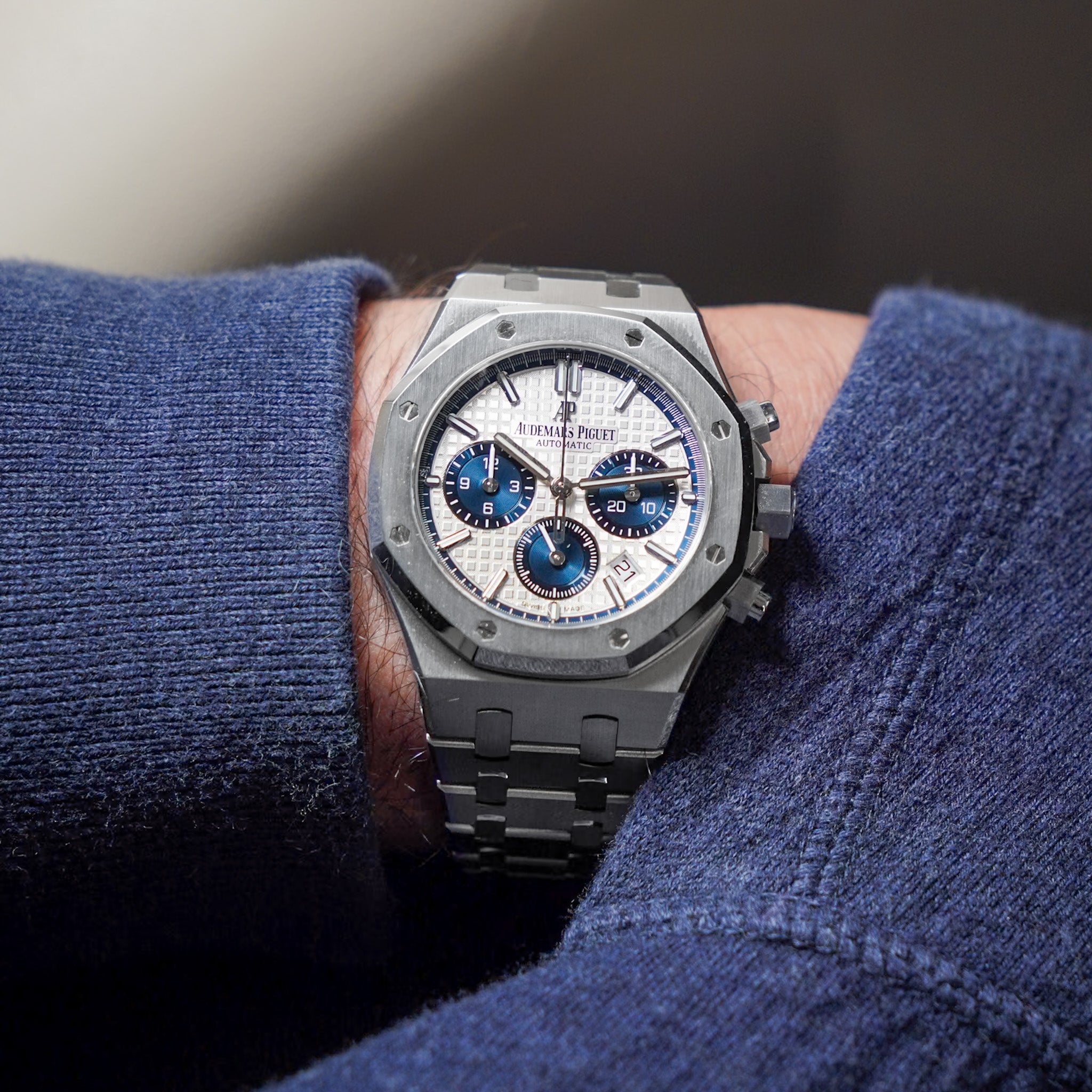 Steel chronograph watch on the wrist of a man wearing a blue hoodie