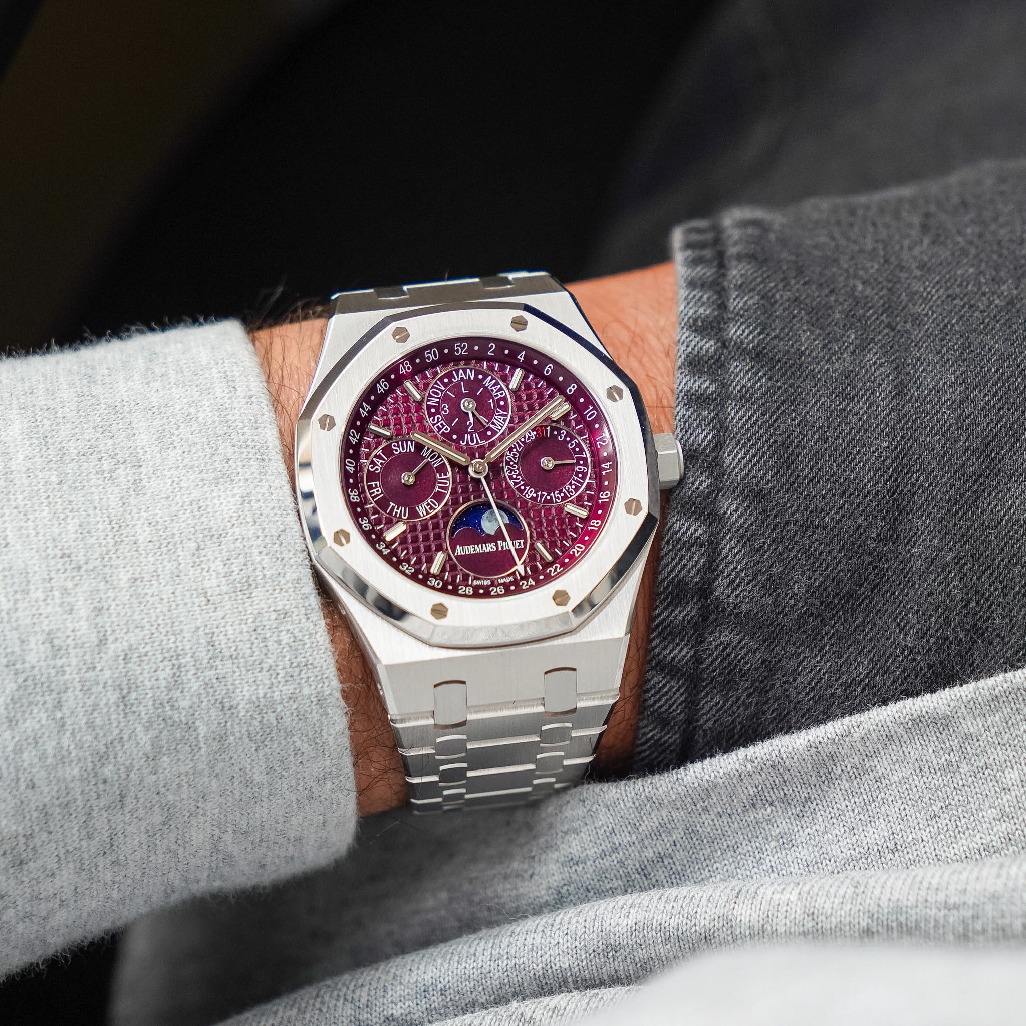 Watch with a red face on a wrist, wearing a gray shirt and jeans.