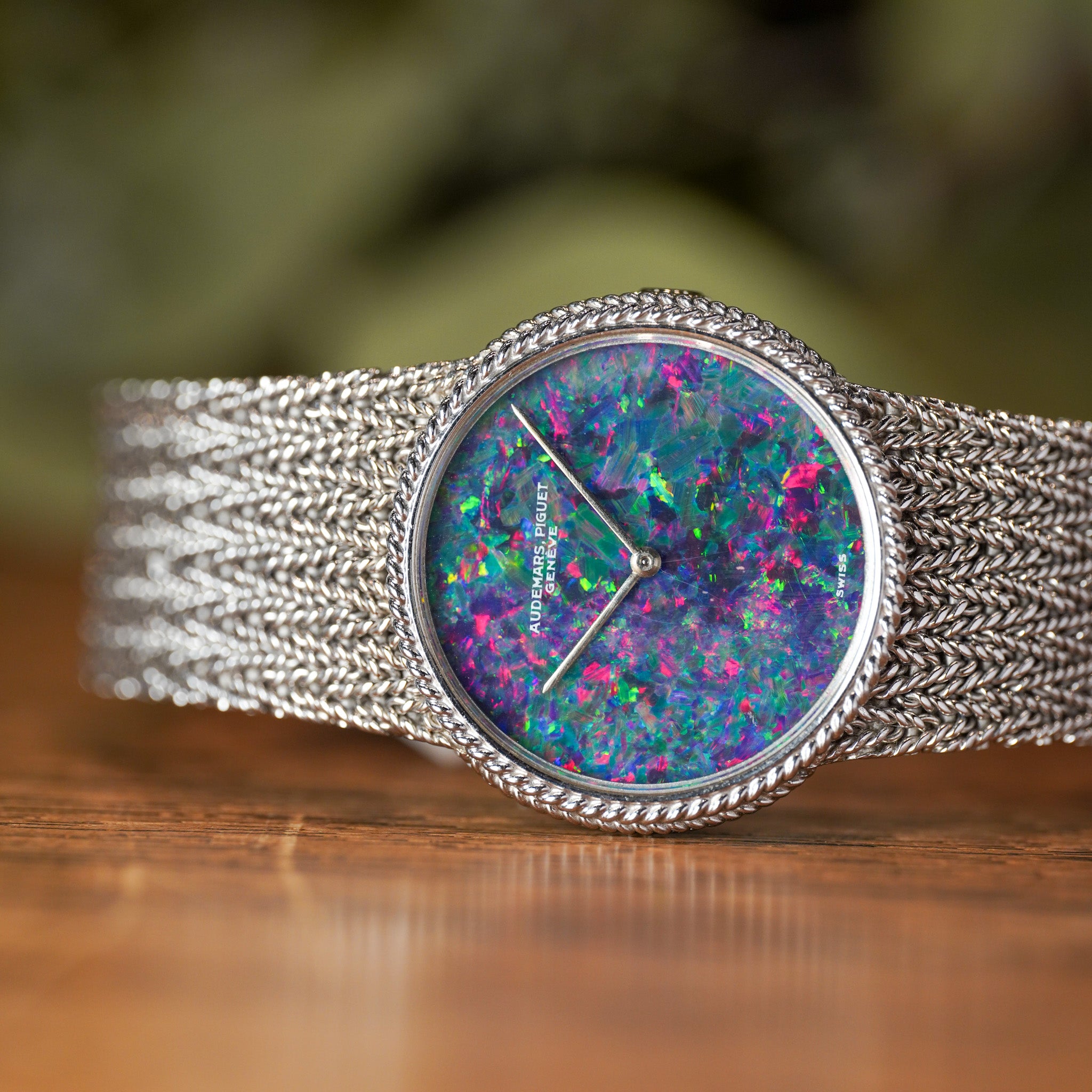 Watch with a colorful face and silver mesh band on a wooden surface