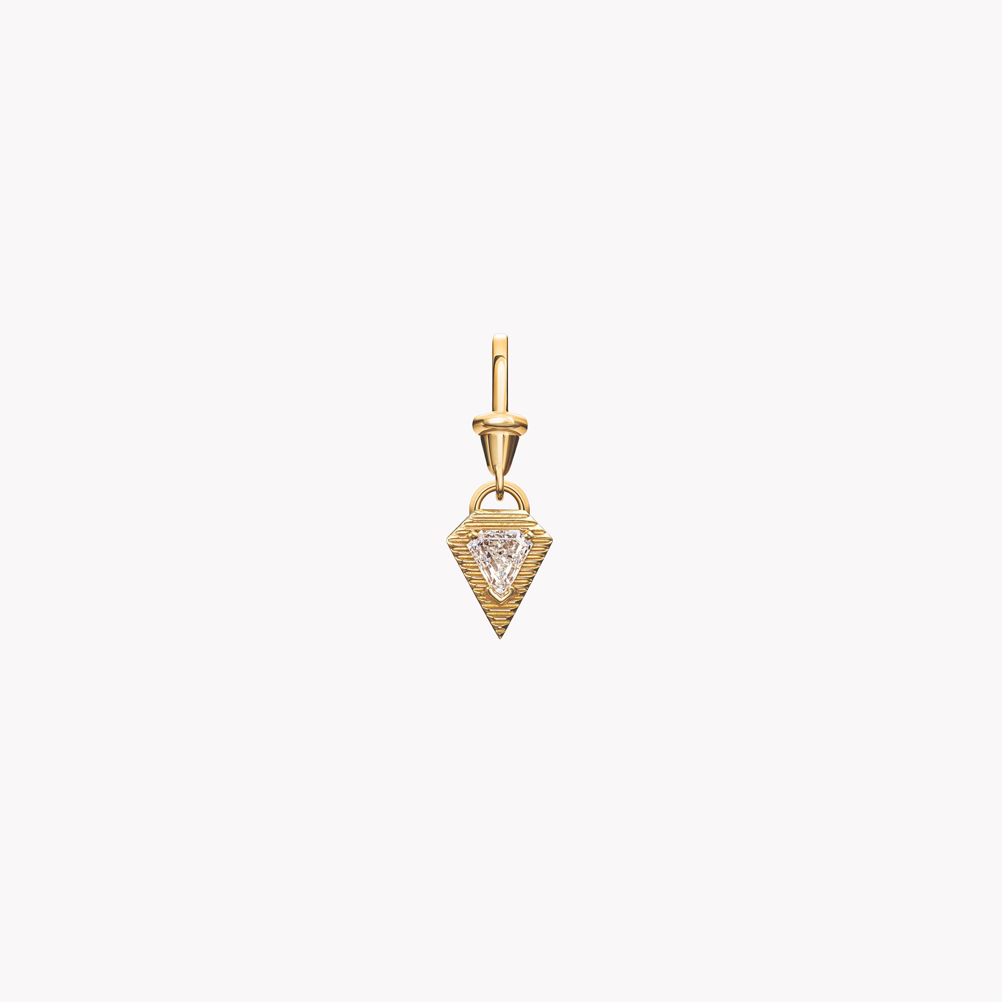 Āzlee Escalier Shield Diamond Charm in 18k yellow gold with a bezel-set trillion-cut diamond, shown on a light coral background.
