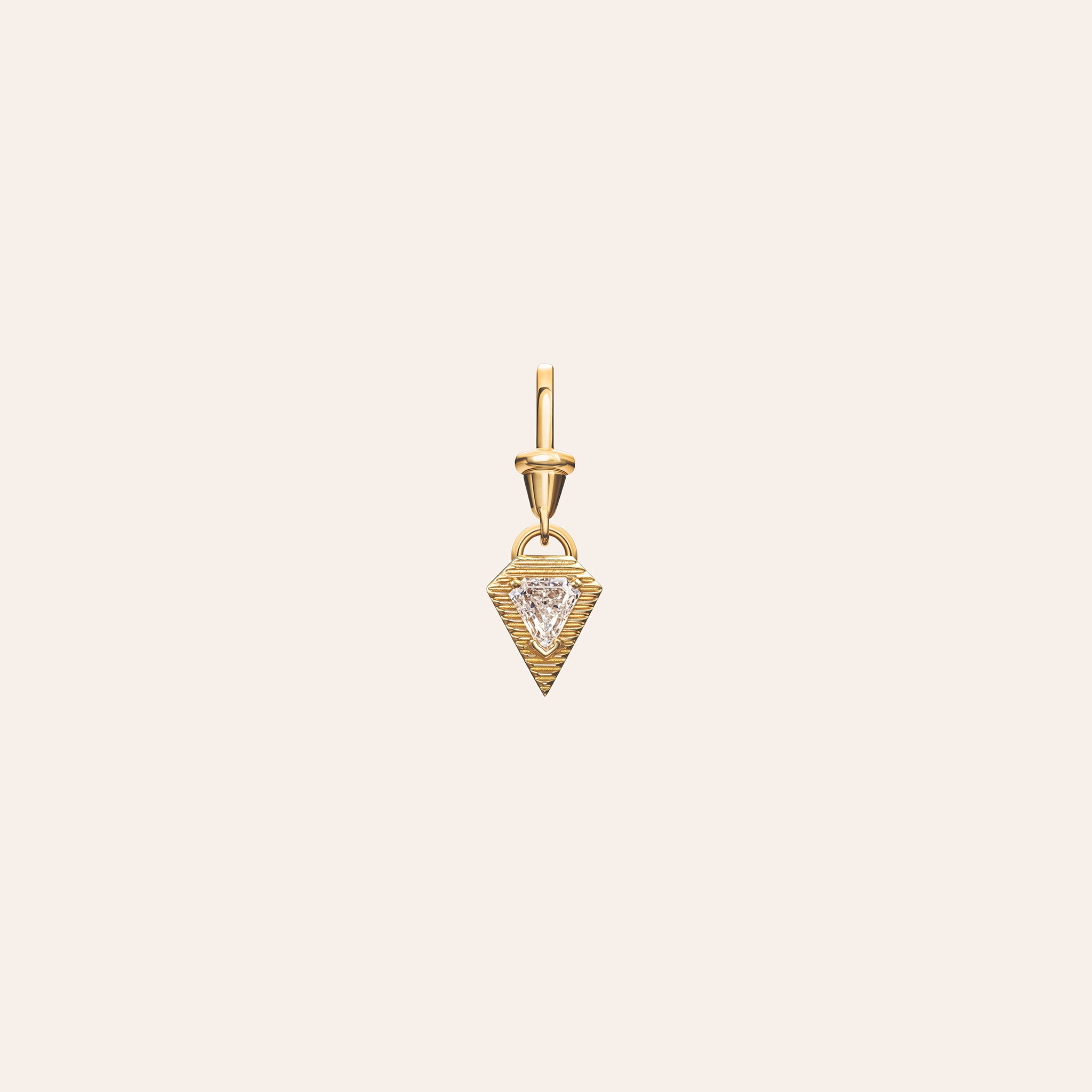 Āzlee Escalier Shield Diamond Charm in 18k yellow gold with a bezel-set trillion-cut diamond, shown on a light coral background.
