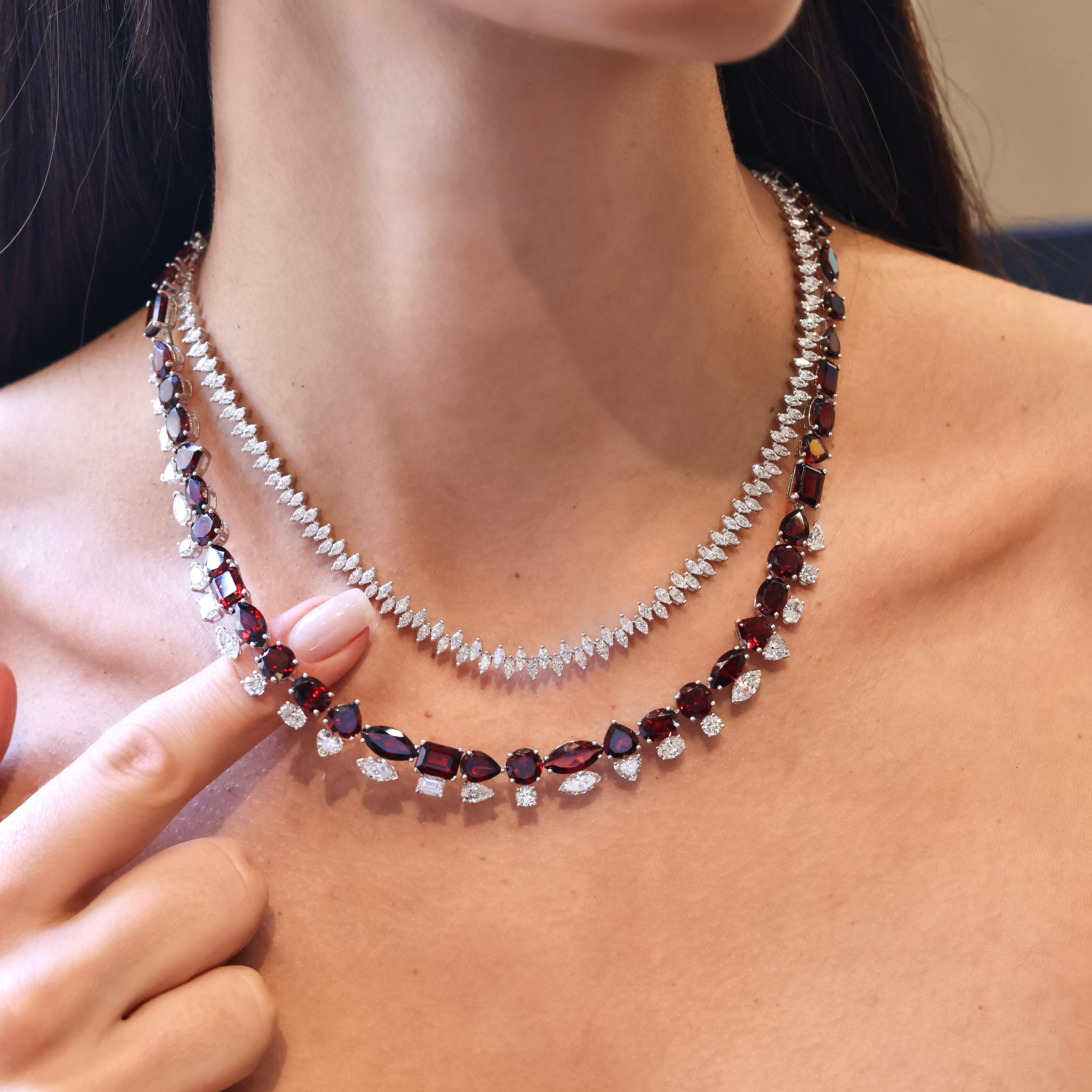 Multi-shape garnet and diamond necklace in 18K white gold featuring vivid deep red garnets totaling 72.96 carats accented by 9.18 carats of white diamonds in a layered tennis-inspired design on model