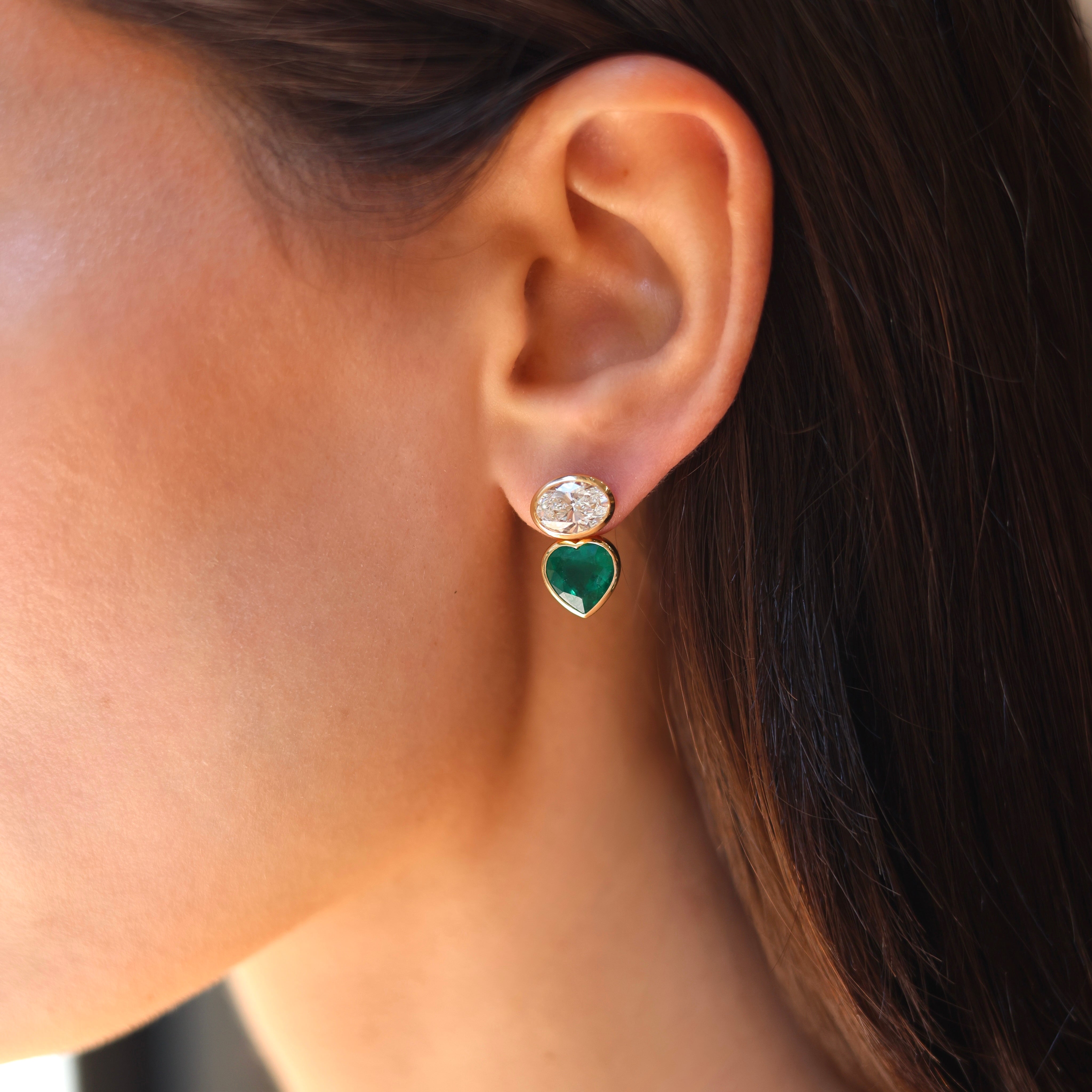 18kt yellow gold stud earrings with bezel-set white oval diamonds and removable heart-shaped emerald jackets, shown assembled and disassembled seen on figure