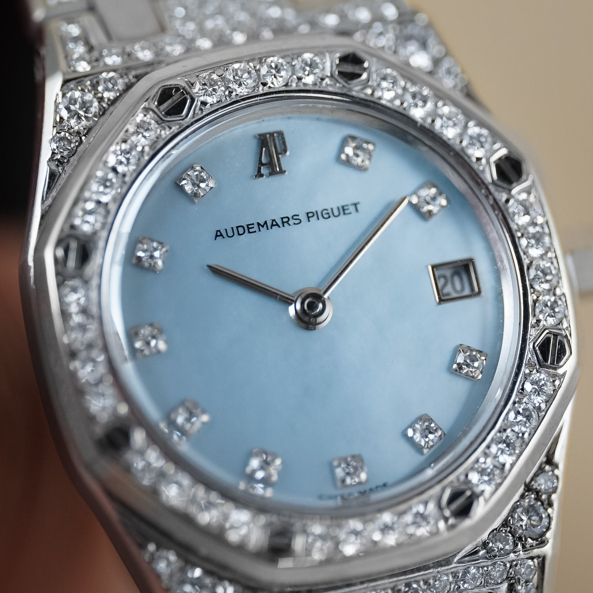 Closeup of a white gold ladies Audemars Piguet Royal Oak with the case bezel, and bracelet covered in diamonds. The dial is mother of pearl. It's shot on a neutral cream background.