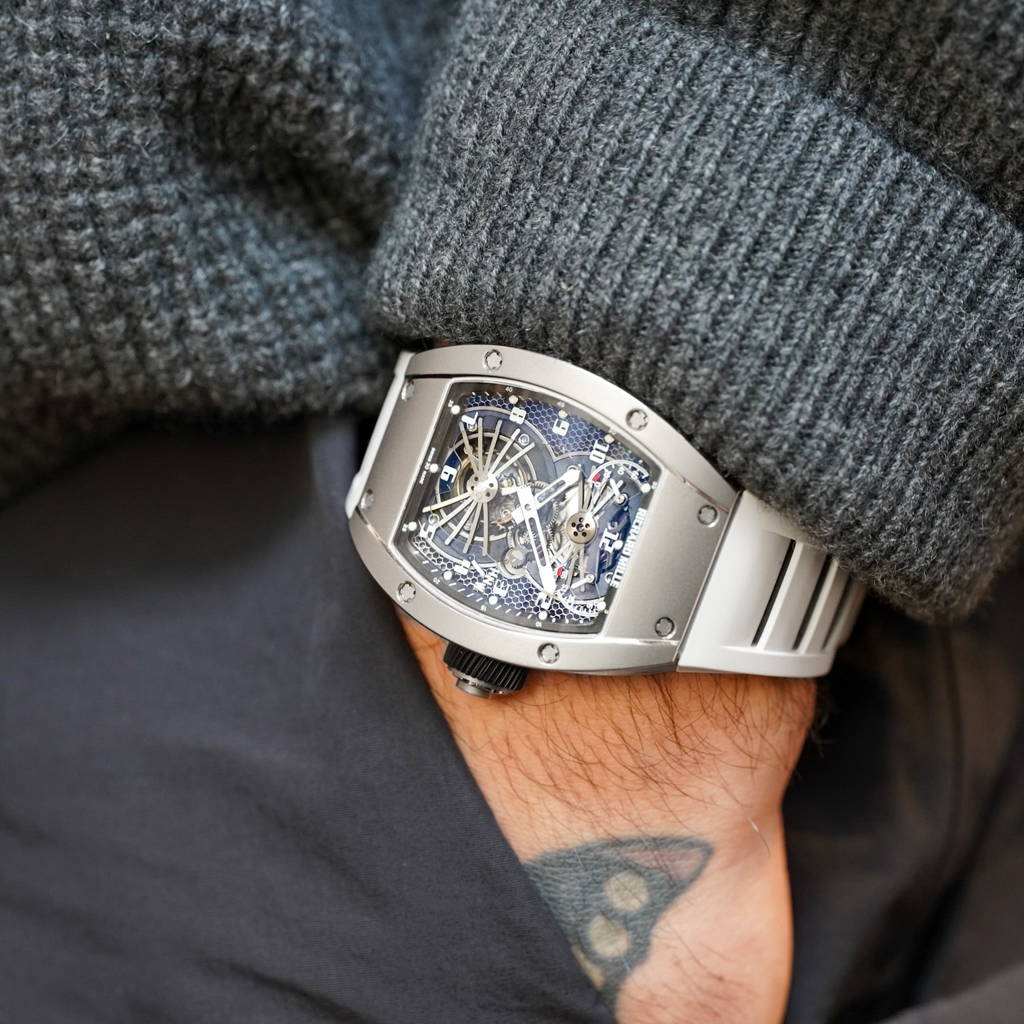 Close-up of a person wearing a silver wristwatch with a textured gray sleeve.
