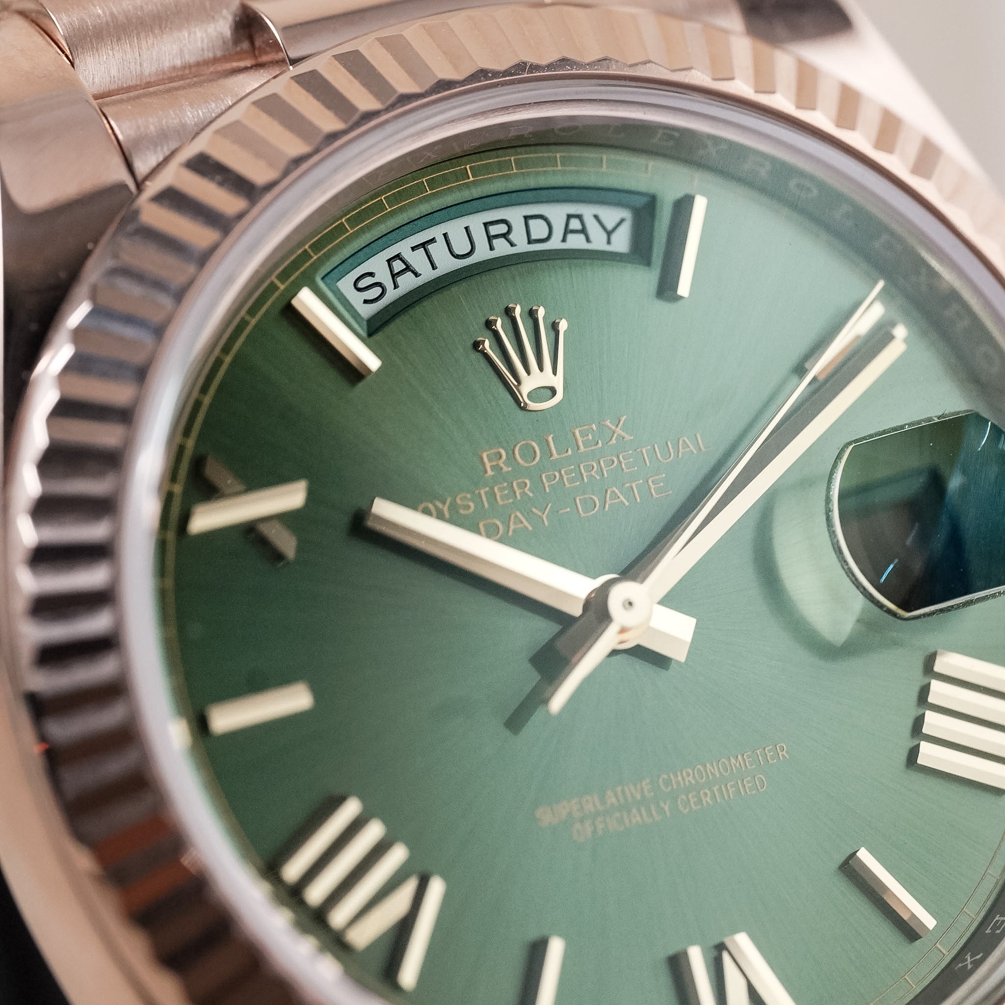Close-up of a Rolex Oyster Perpetual Day-Date watch with a green dial, rose gold case, fluted bezel, and day-of-week window at the top.