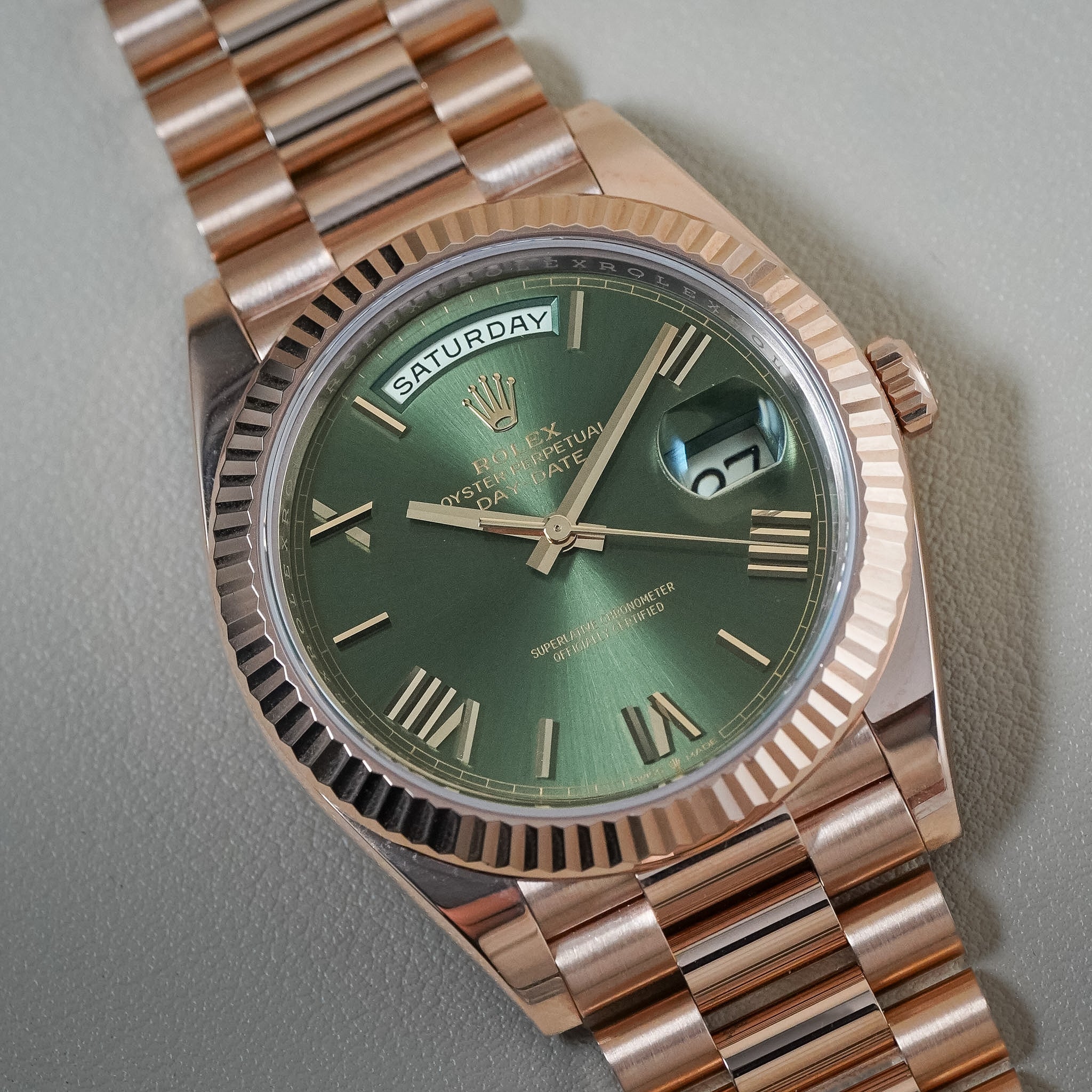 A Rolex Datejust wristwatch with a green sunburst dial, rose gold case, and matching rose gold Oyster bracelet, photographed close-up on a neutral gray background.