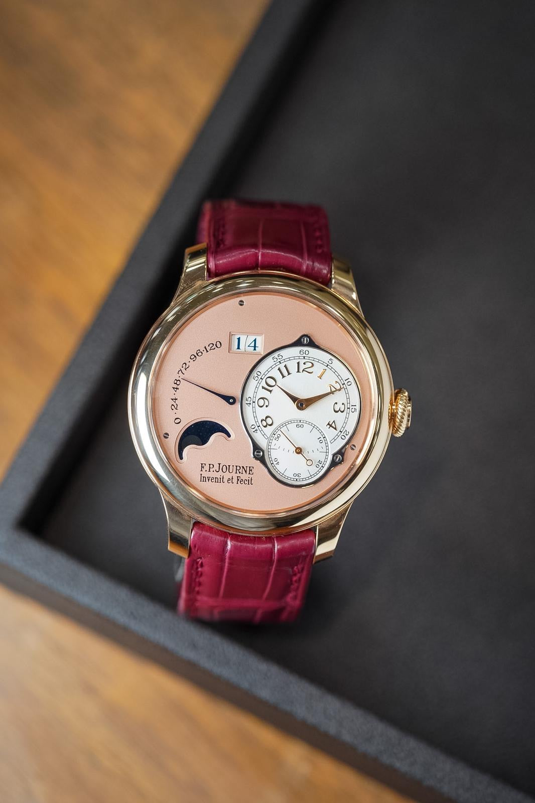 Luxury watch with pink face and red leather strap on a dark surface