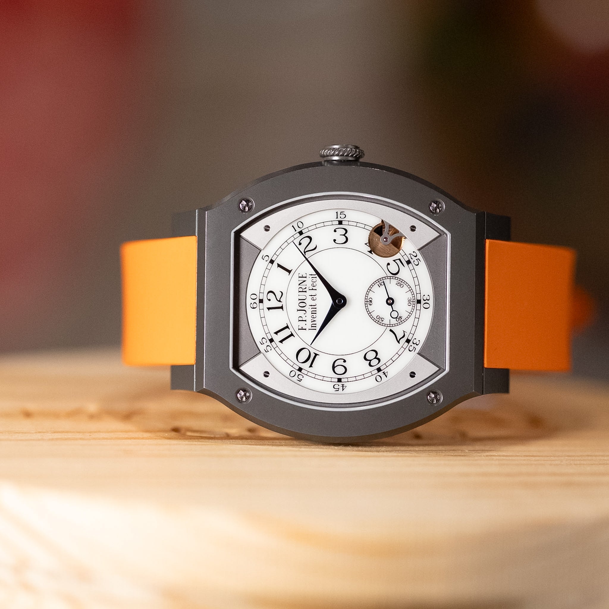 Titanium watch with an orange strap sideways on a table