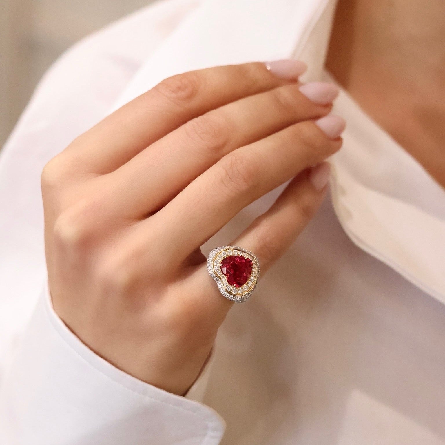 Close-up of a hand wearing a ring with a red gemstone against a blurred background.