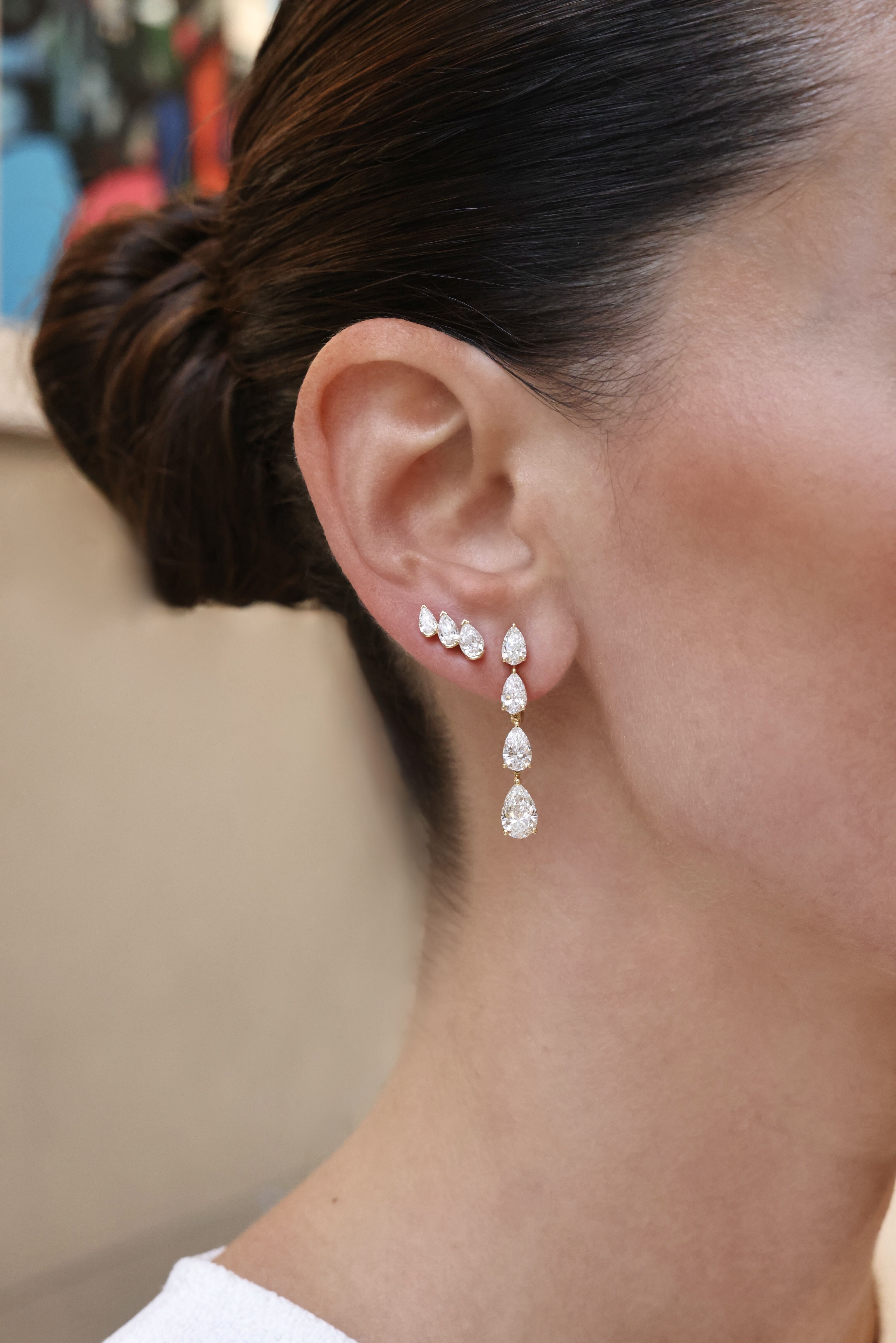 Close-up of pear-shaped diamond climber studs worn alongside a graduated pear diamond drop earring in 18K yellow gold