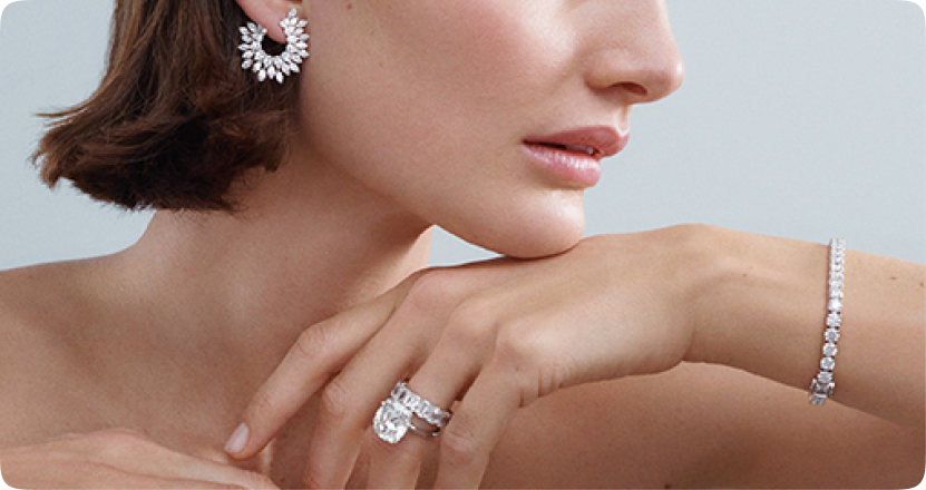 profile of a woman whose chin is resting on her hand, displaying diamond earrings, stacked rings, and a bracelet