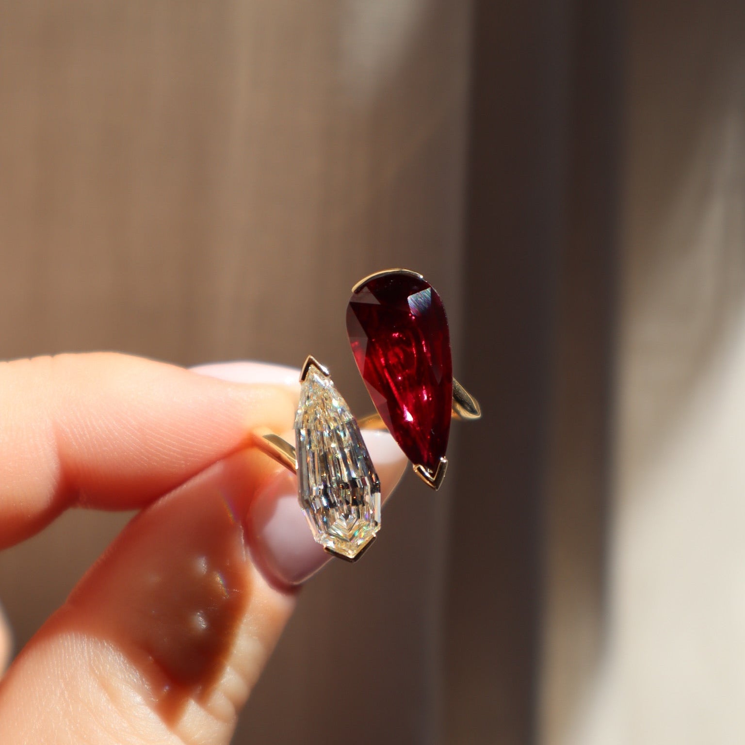 Two gemstones, one red and one clear, held between fingers against a neutral background.