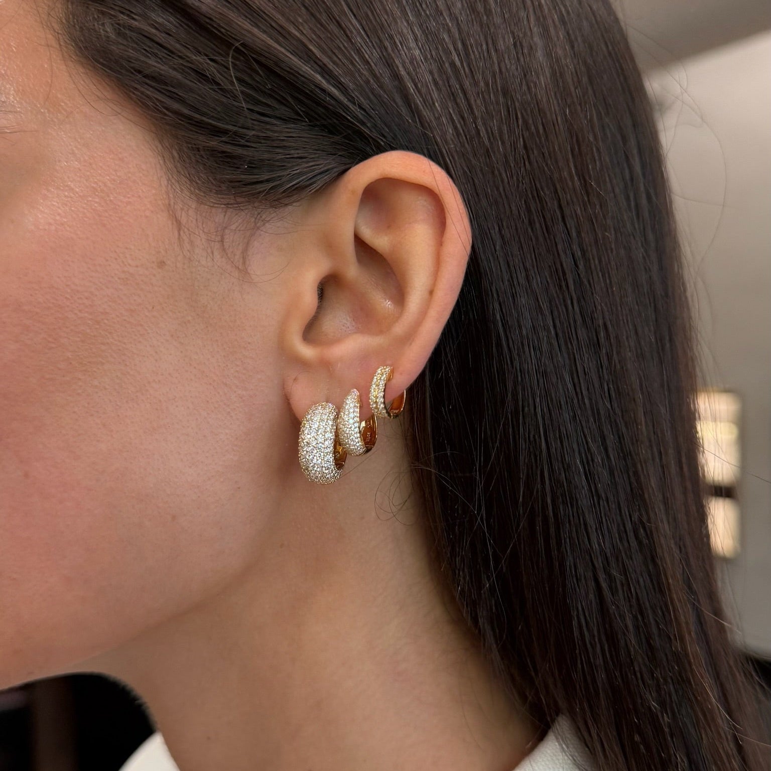Close-up of a person wearing diamond hoop earrings with a blurred indoor background