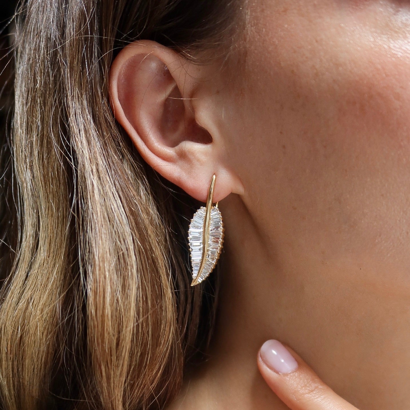 Close-up of a person wearing a gold leaf-shaped earring.