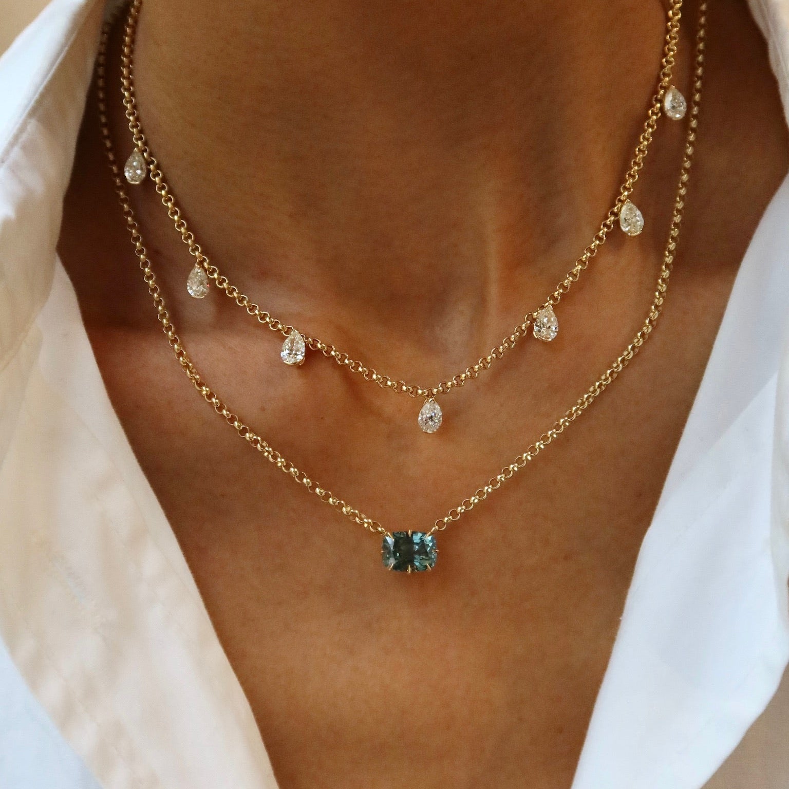 Close-up of a person wearing a gold necklace with a green gemstone on a white shirt.