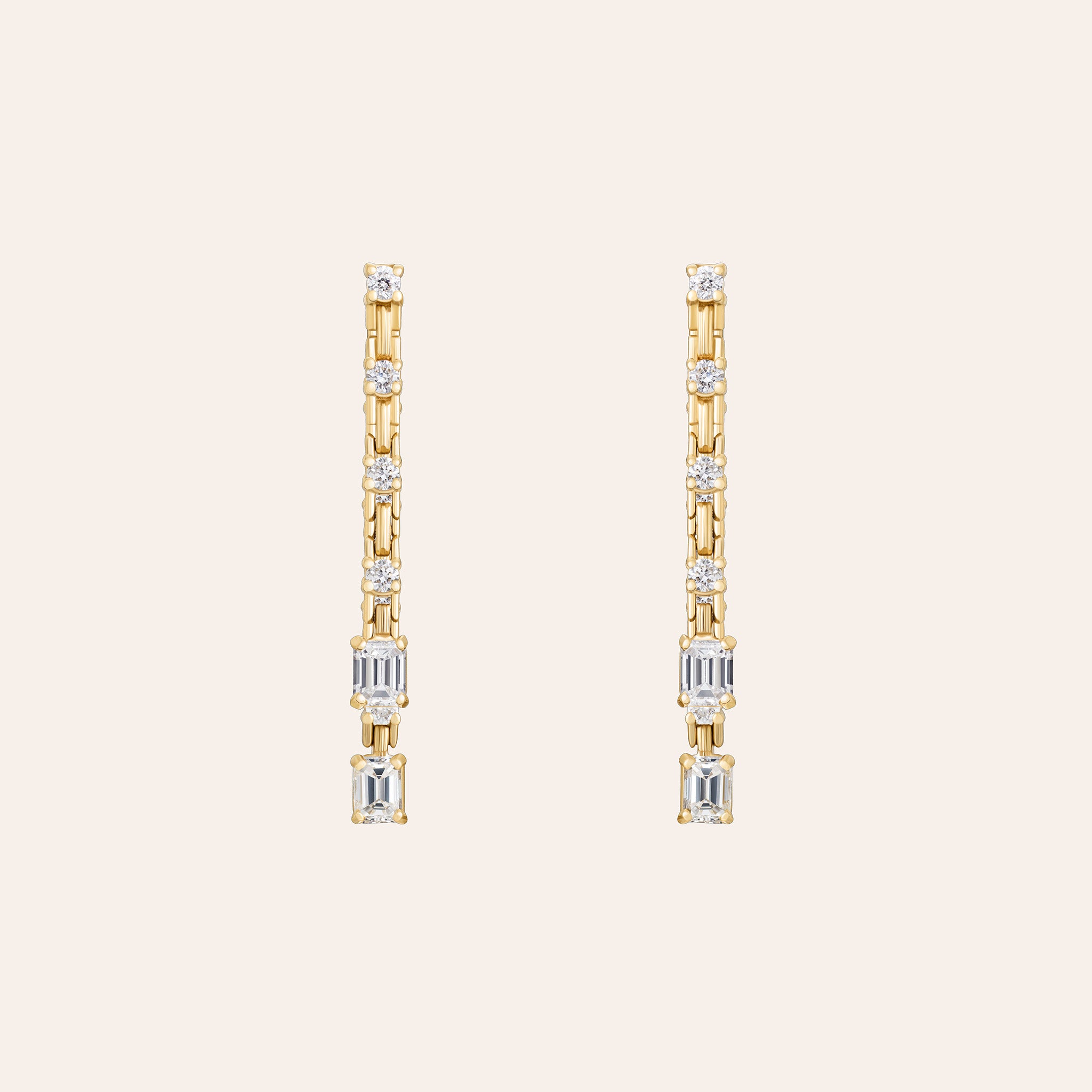 A pair of yellow gold drop earrings with emerald and round-cut diamonds, displayed on a solid light beige background.