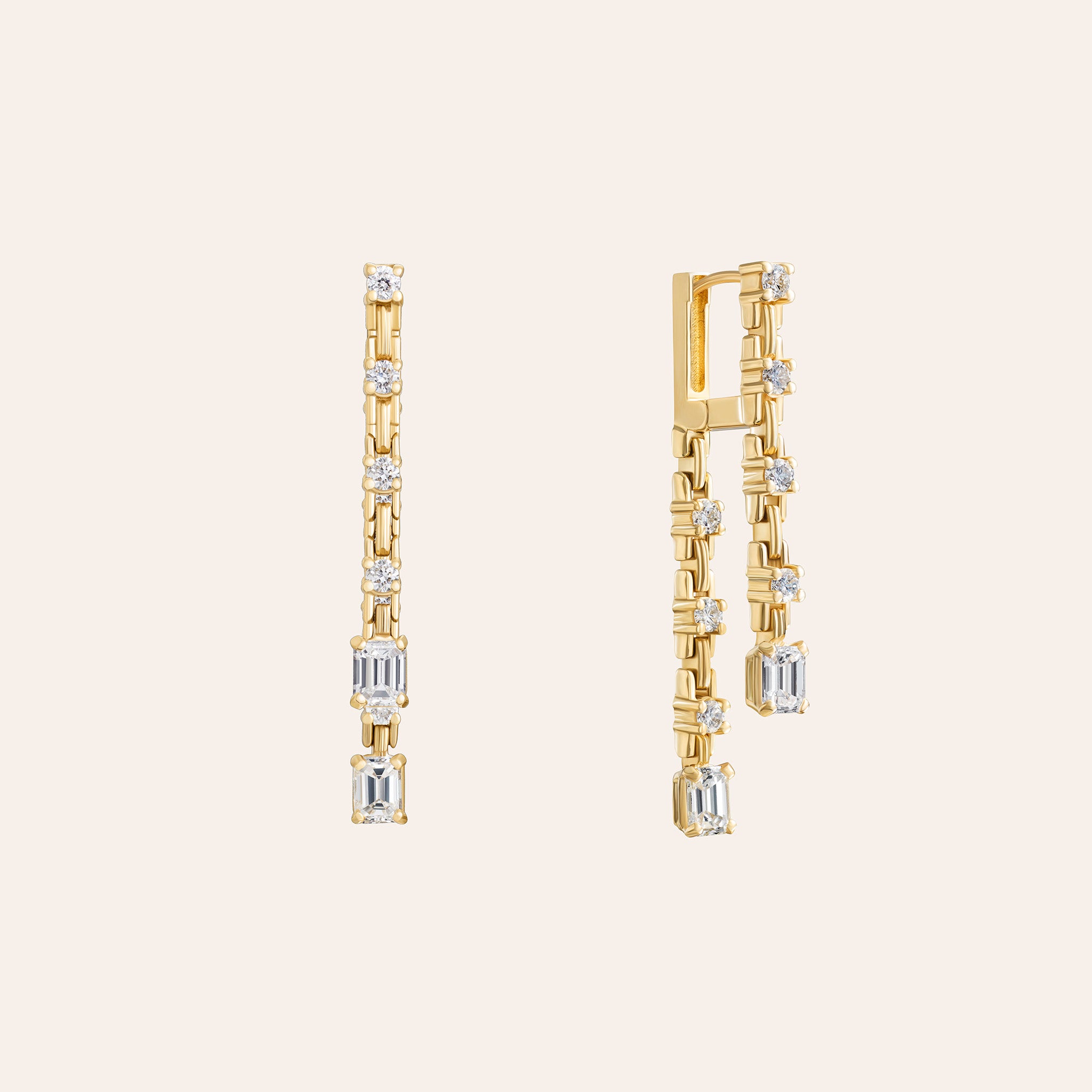 A pair of yellow gold dangle earrings with emerald and round-cut diamonds displayed on a light cream background.