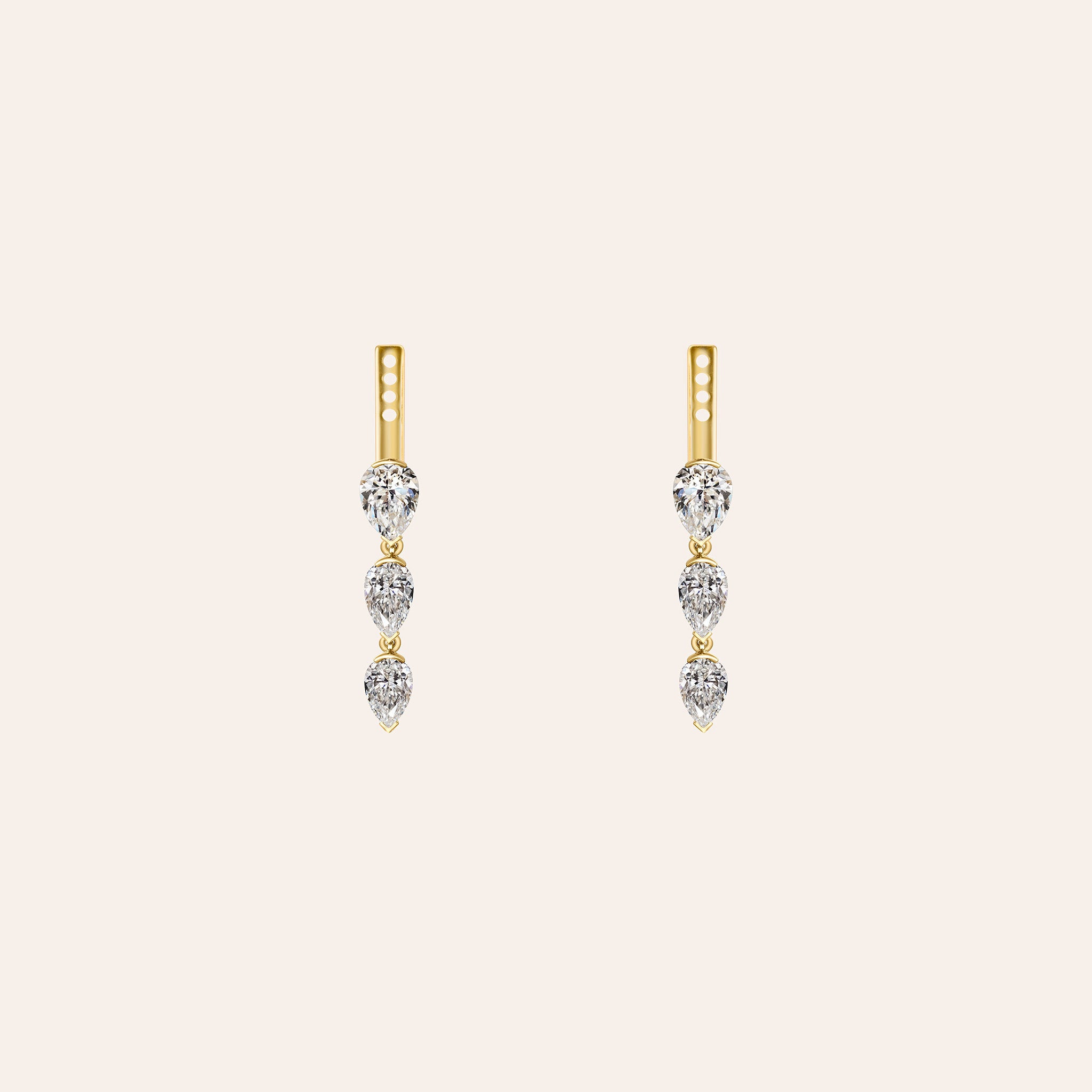 A pair of gold drop earrings with three clear pear shape diamonds in each earring, displayed on a light cream background.