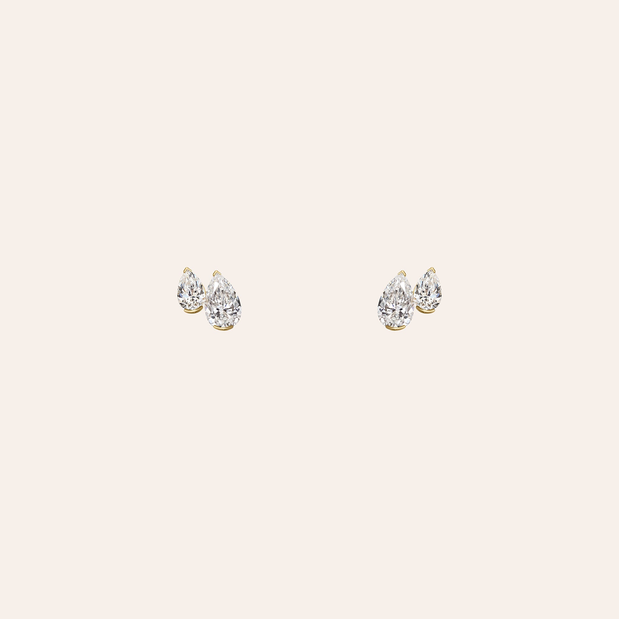 A pair of yellow gold set duo pear shaped diamond stud earrings displayed on a solid light beige background.