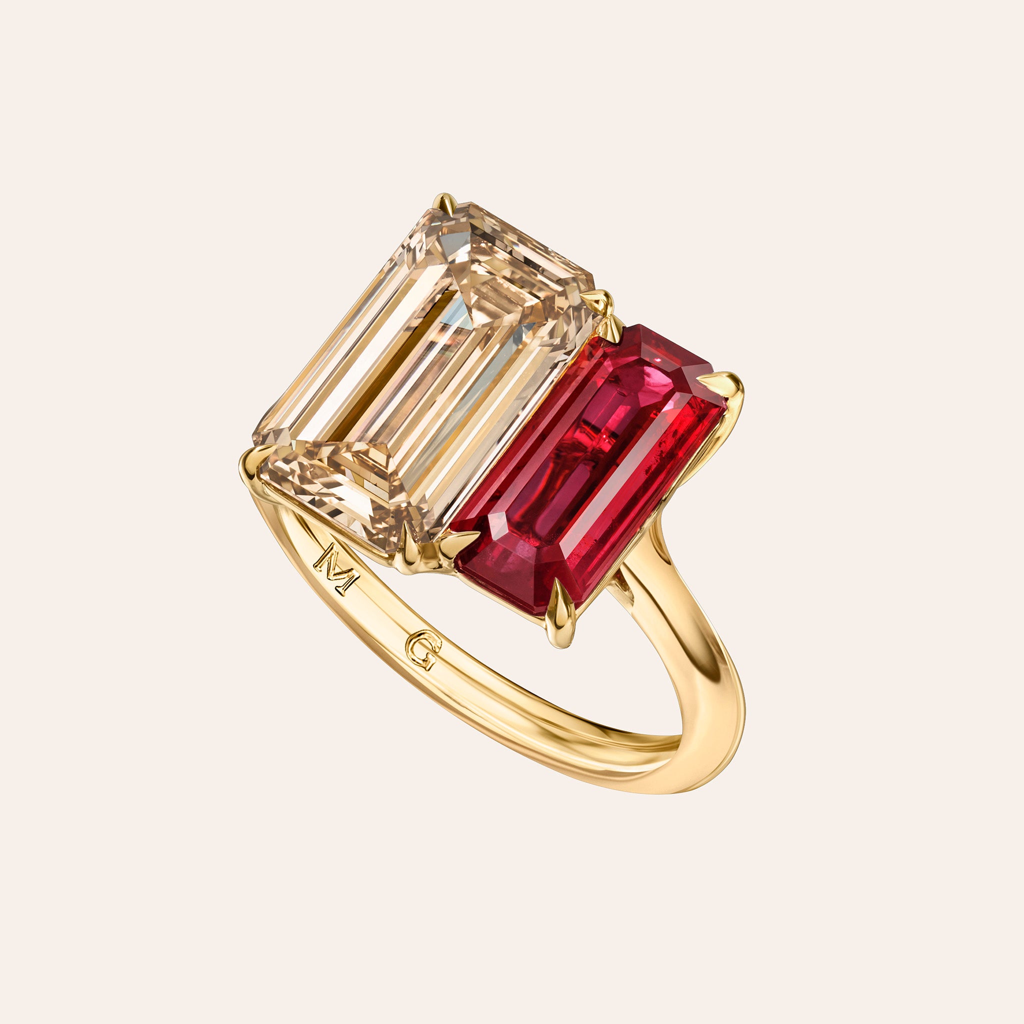 A2: Angled view of an 18K yellow gold toi et moi ring with a fancy yellow-brown emerald-cut diamond and vivid red ruby, showing the MG signature engraving on the polished gold shank.
