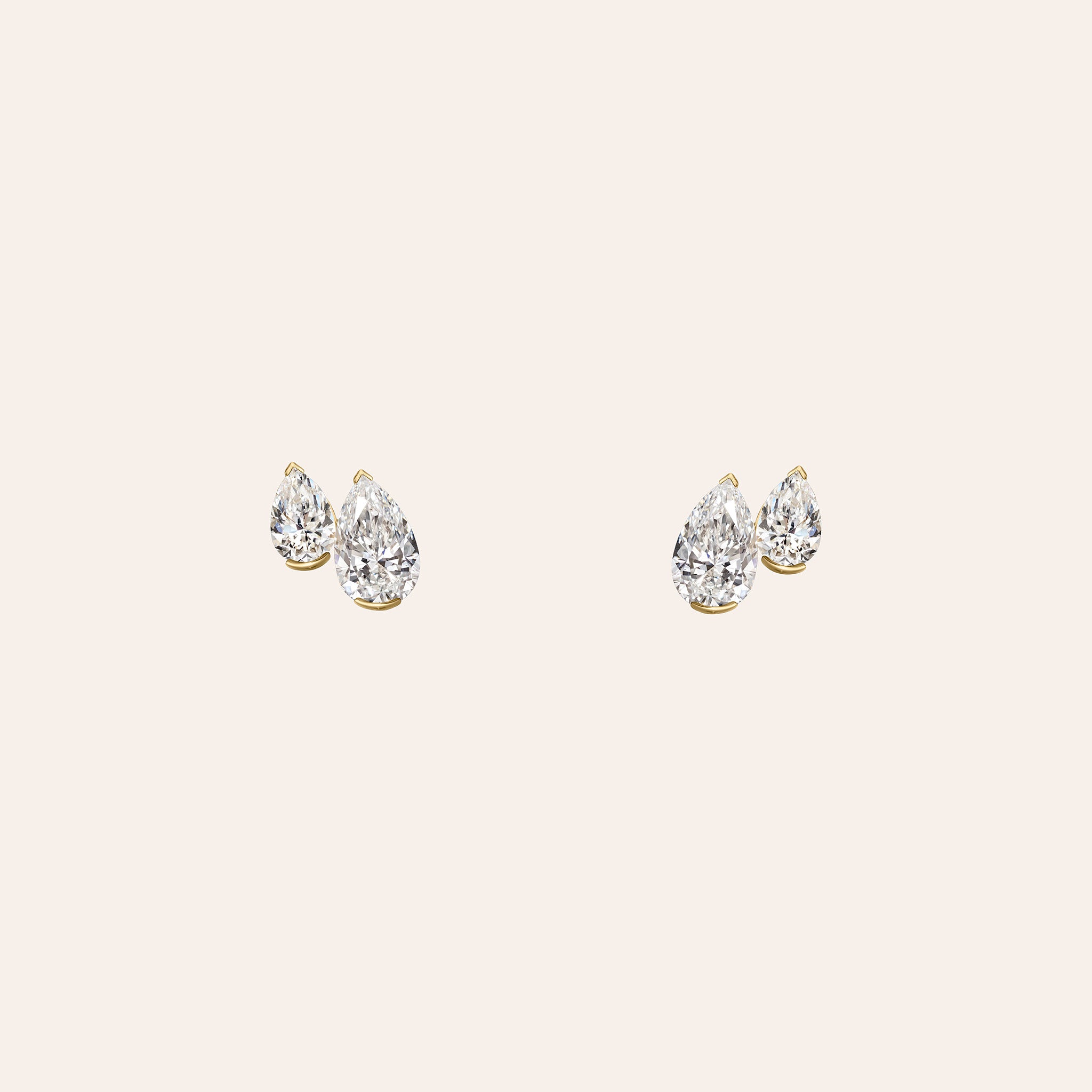 A pair of gold stud earrings featuring two pear-cut diamonds, displayed on a solid light beige background.