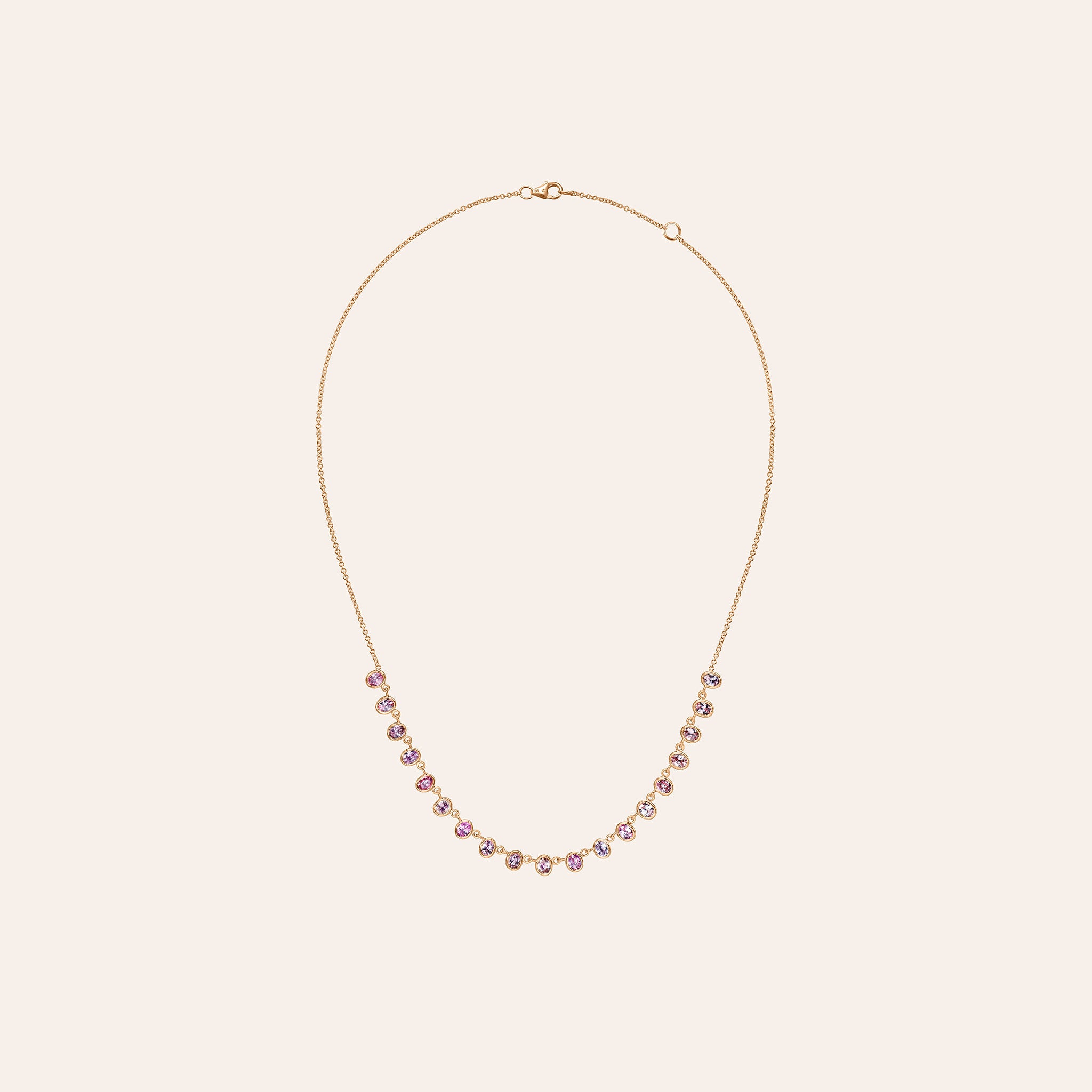 The Lena Pink Sapphire Necklace in 14K rose gold, with eyeglass-set oval pink and purple sapphires linked along the chain, shown against a cream background.