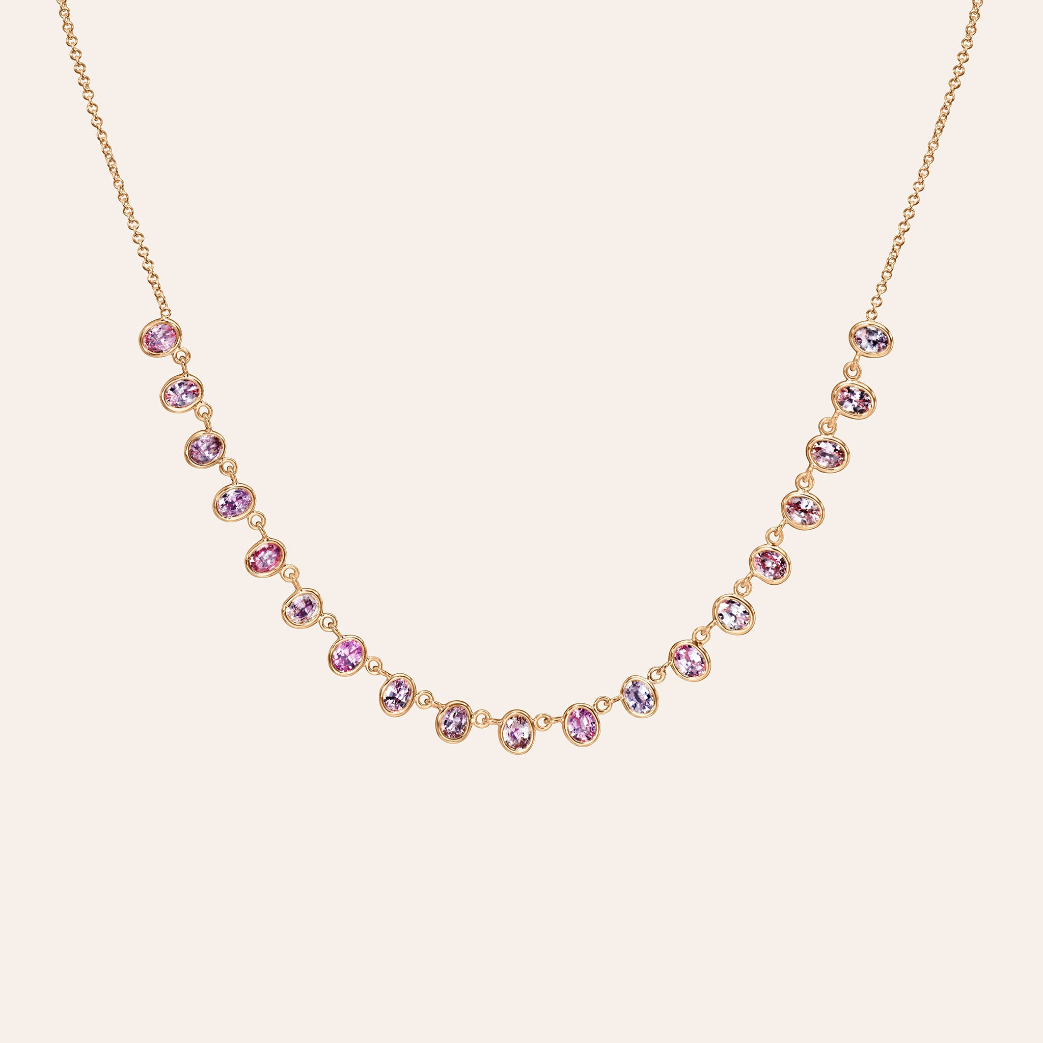 Alternate view of The Lena Pink Sapphire Necklace in 14K rose gold, showing oval pink and purple sapphires in eyeglass settings, against a cream background.