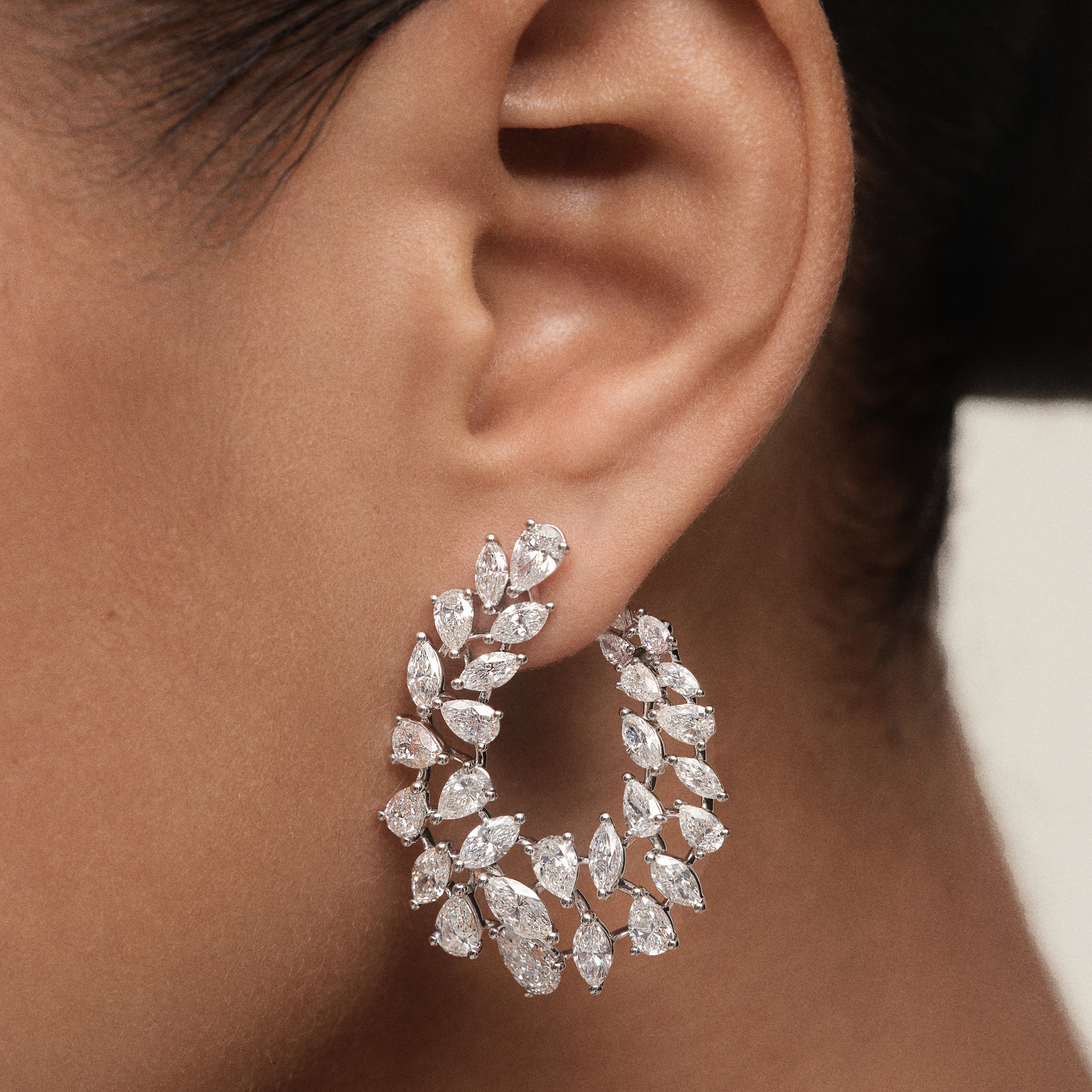Open hoop earring in 18K gold with individually placed pear and marquise-cut diamonds in a scattered arrangement on ear